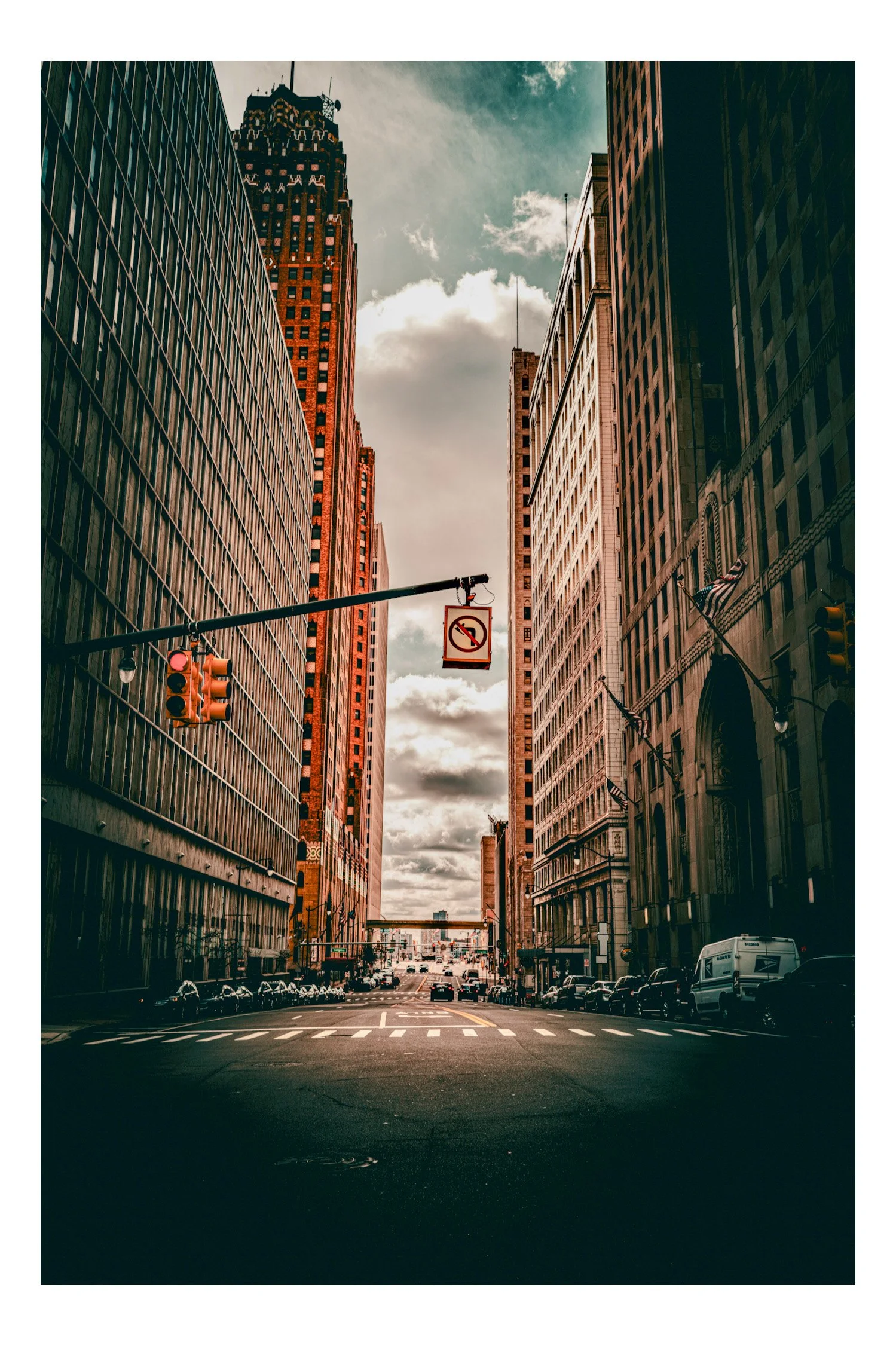 City street scene with tall skyscrapers, traffic signal, no U-turn sign, and parked cars, under a cloudy sky.