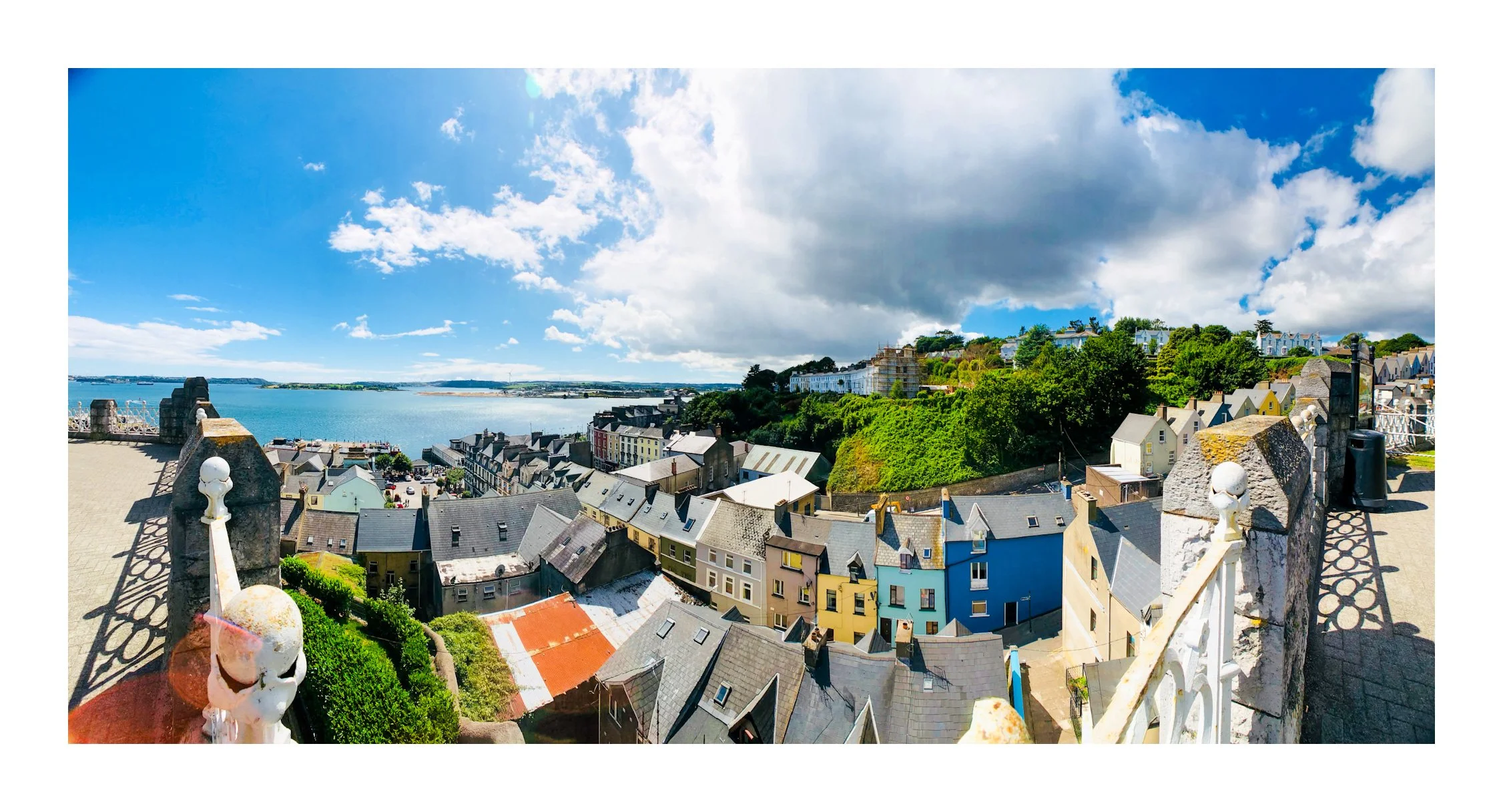 Panoramic view of a coastal town with colorful houses, a large body of water, and a partly cloudy sky.