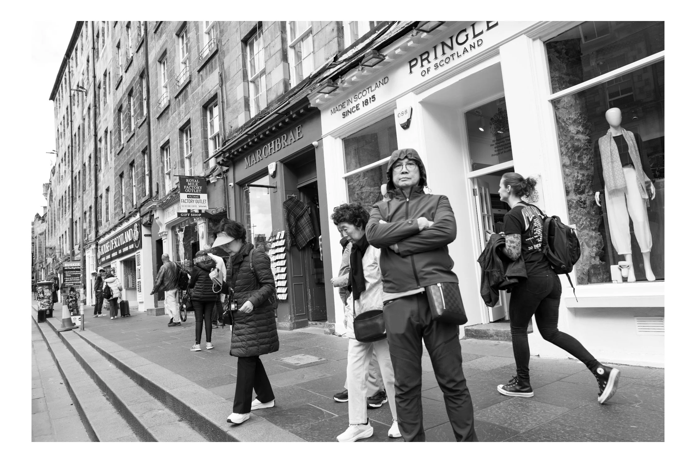 People walking on a city sidewalk in front of clothing stores, black-and-white photo
