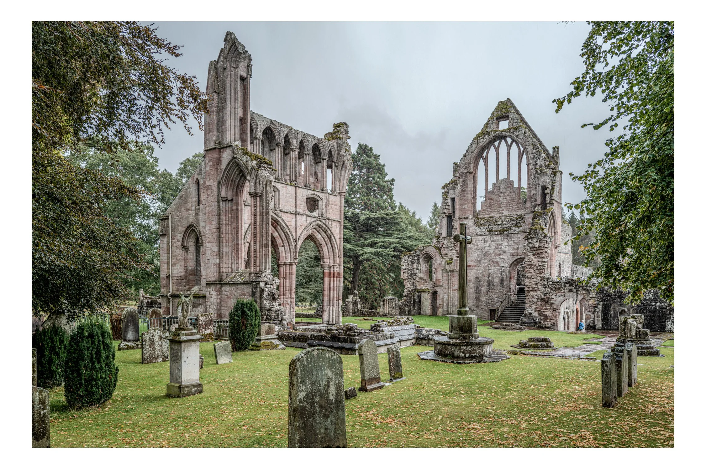 Ruins of an old stone church with arched windows and doorways, surrounded by gravestones and greenery.