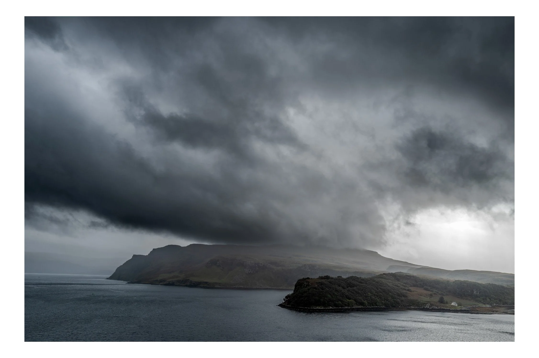 Rugged coastline with dark clouds overhead and a body of water in the foreground.