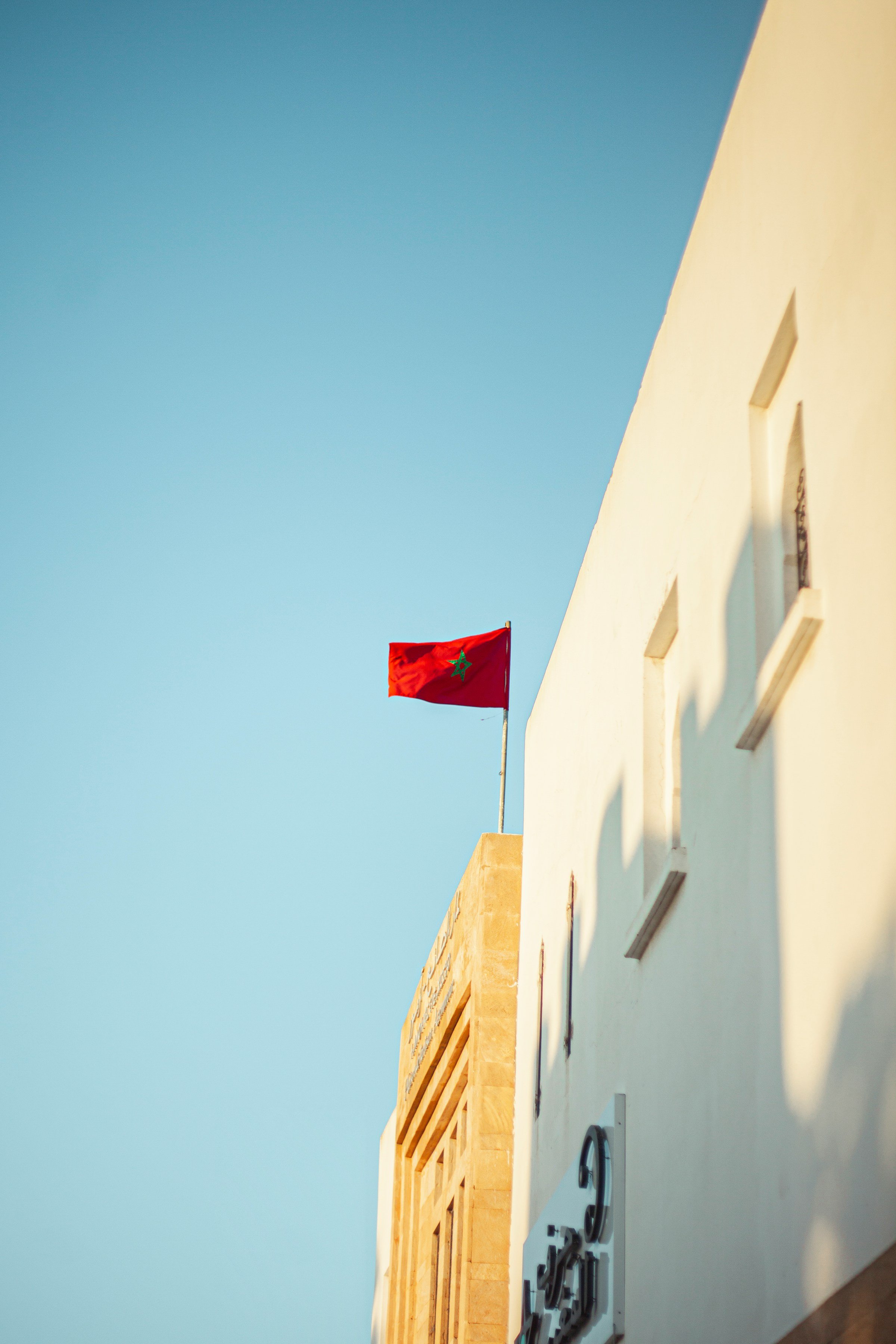 A red flag with a green star flying atop a building with white walls and windows under a clear blue sky.