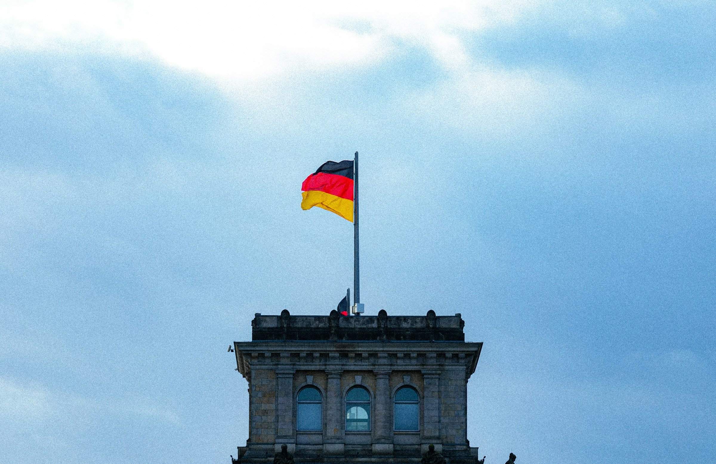 German flag flying atop a historic stone building against a partly cloudy sky.