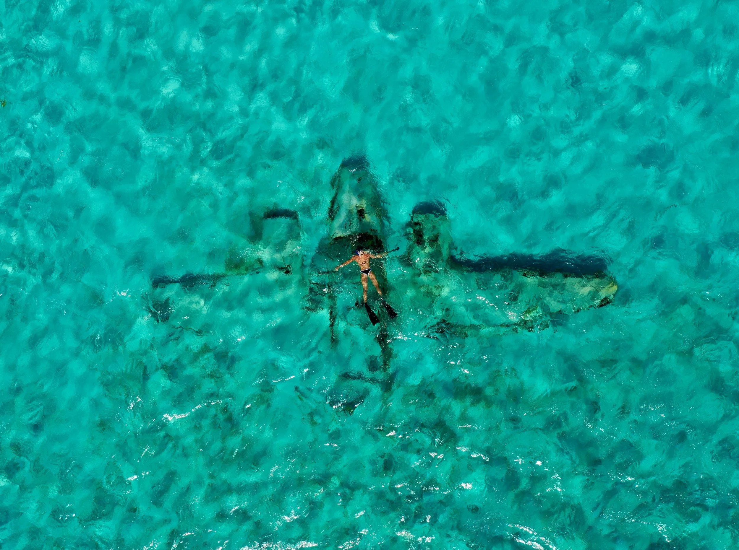 A person in a swimsuit floating on a jet ski submerged in clear turquoise water, surrounded by several other jet skis.