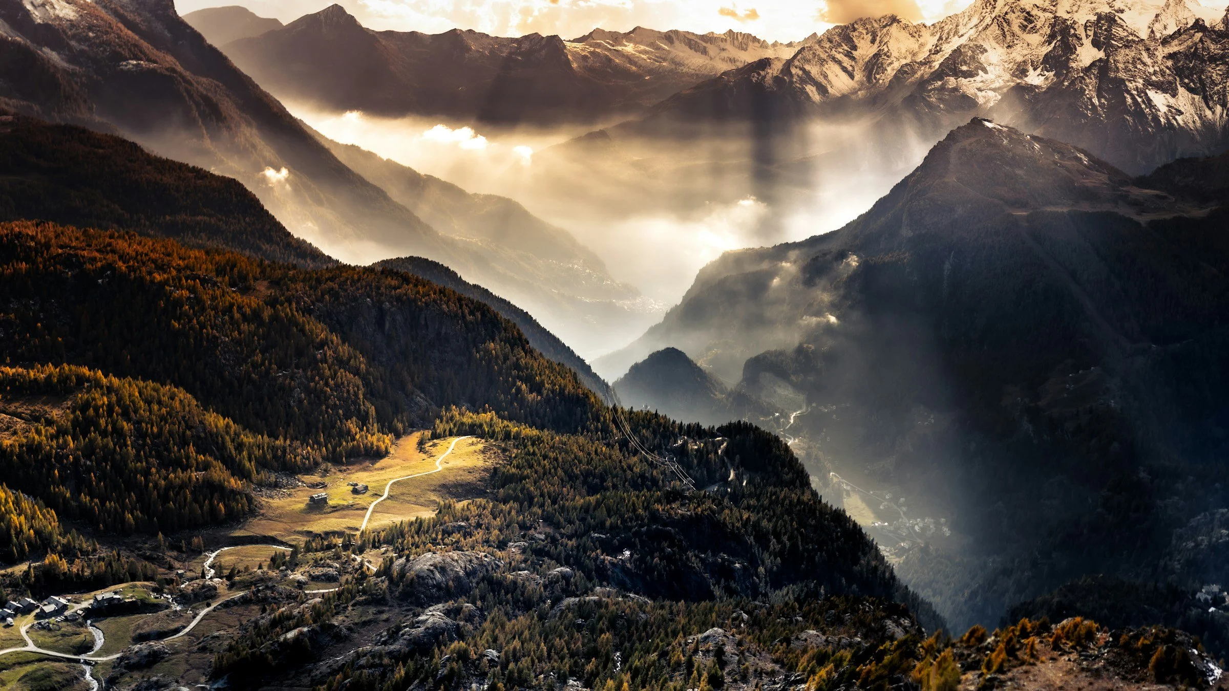 Aerial view of a mountain landscape at sunset with valleys, forests, and small houses.