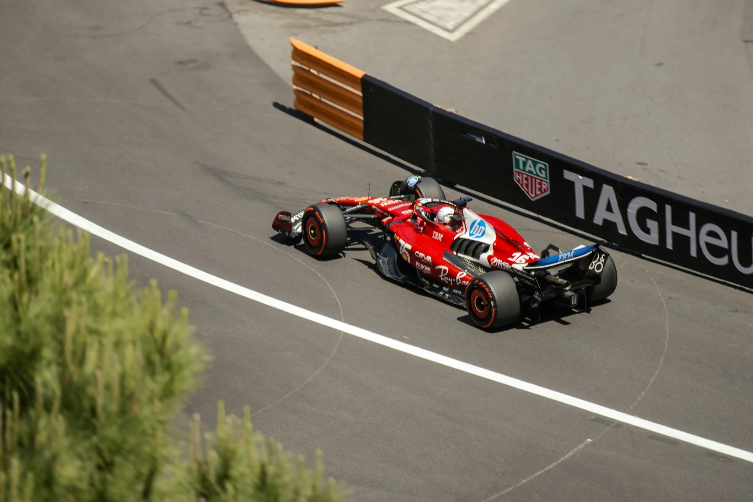 A red Formula 1 race car on the track, with the driver's helmet visible as they navigate a turn near a wall with TAG Heuer branding.
