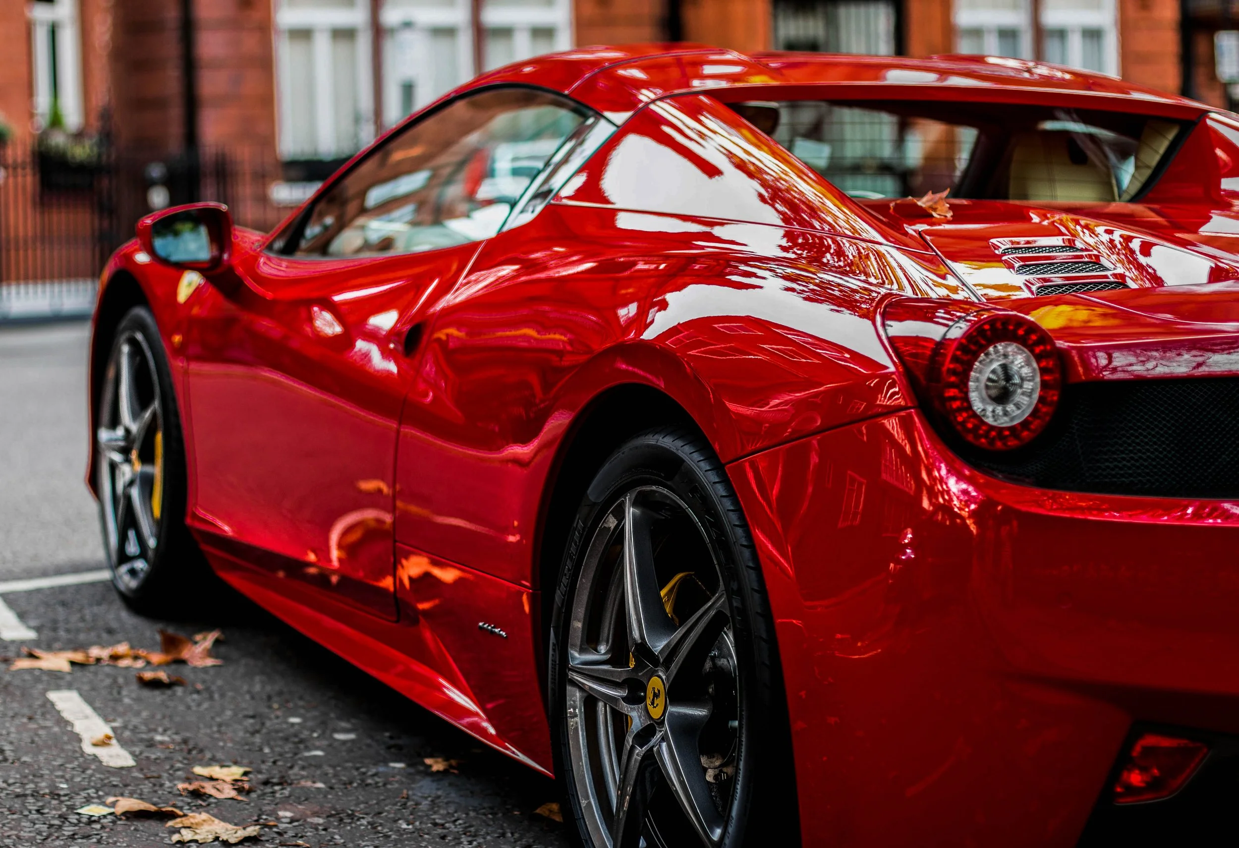 A red sports car parked on a city street with fallen leaves on the ground.