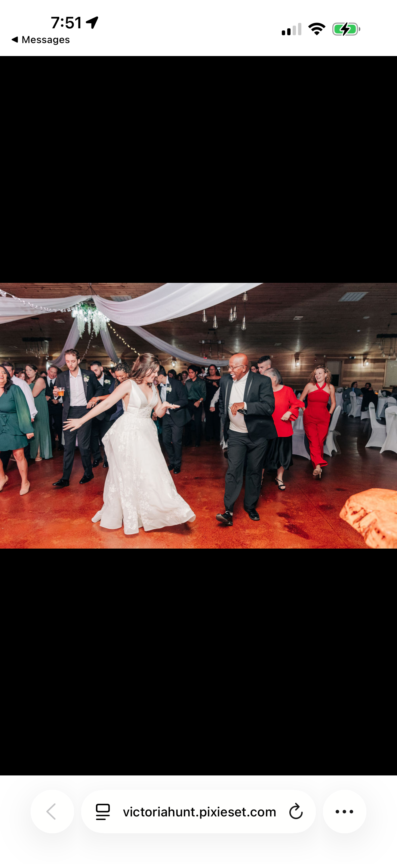 People dancing at a wedding reception inside a decorated venue with white drapery and hanging lights.