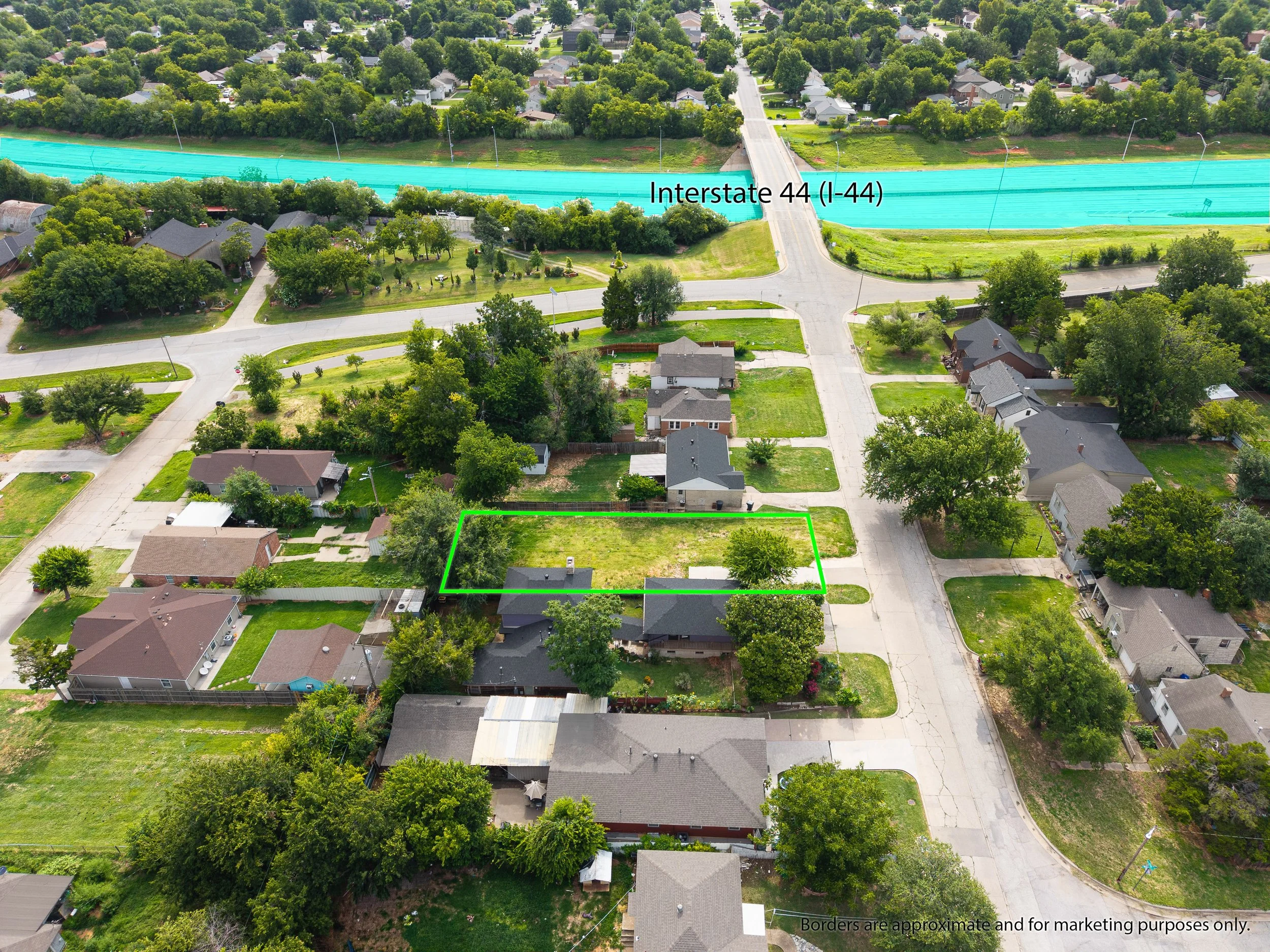 Aerial view of a residential neighborhood showing houses, trees, and streets, with a highway labeled Interstate 44 (I-44) running horizontally across the image. A green boundary marks a specific property lot in the foreground. OKC Drone