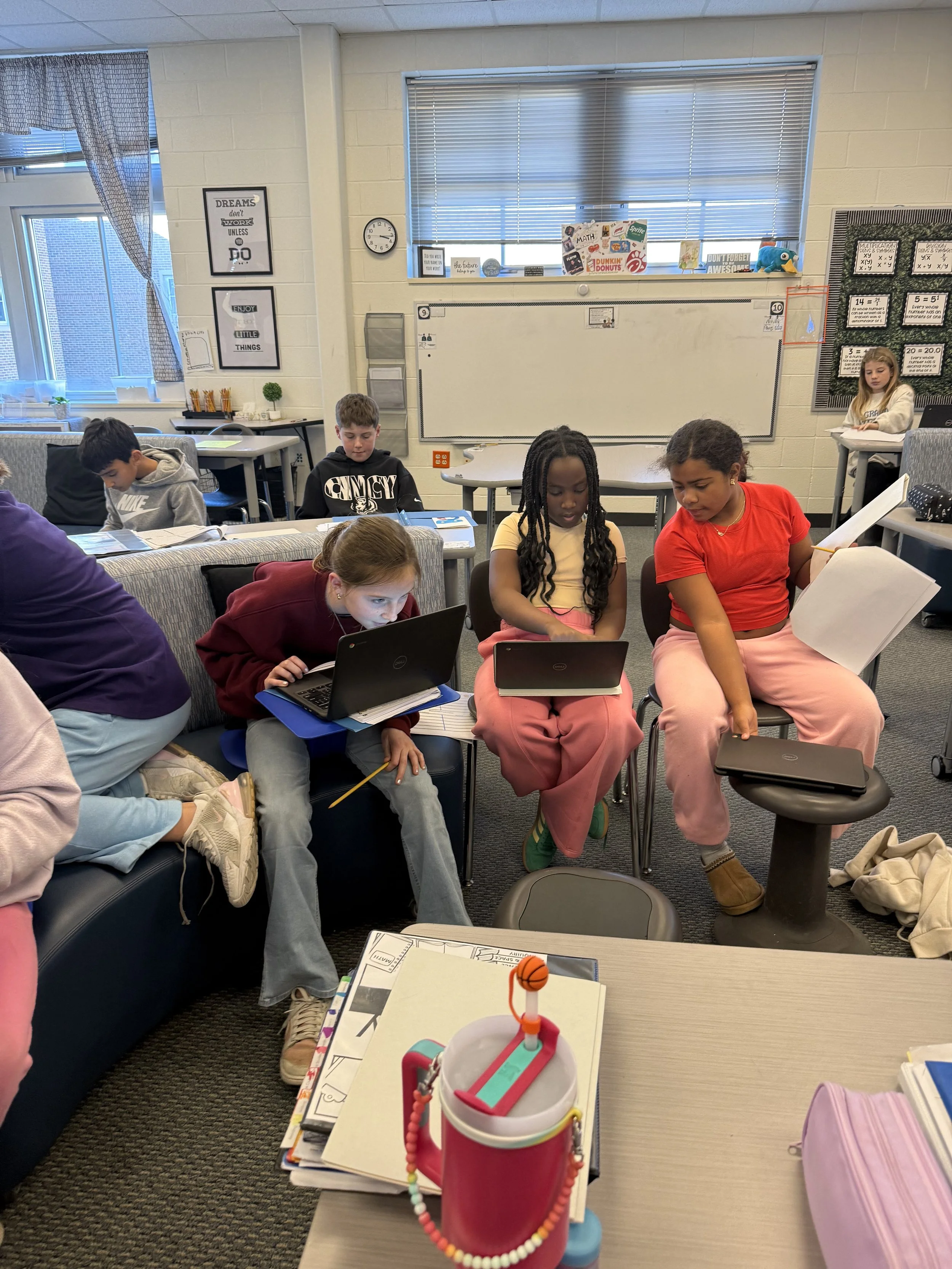 Students using laptops in a classroom with posters and decorations on the wall.