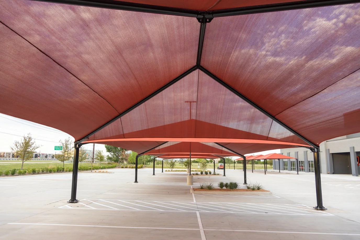 Empty parking lot with two large red canopy shades and some small landscaping plants.