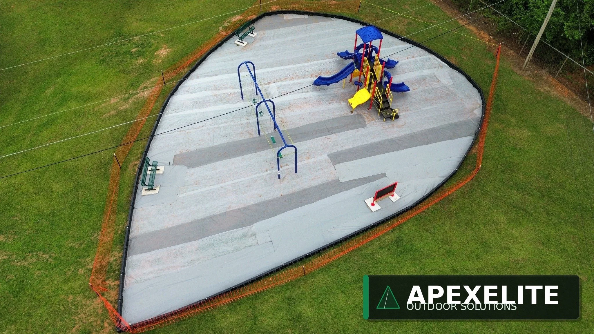 A playground with slides and swings surrounded by a safety net and grass.