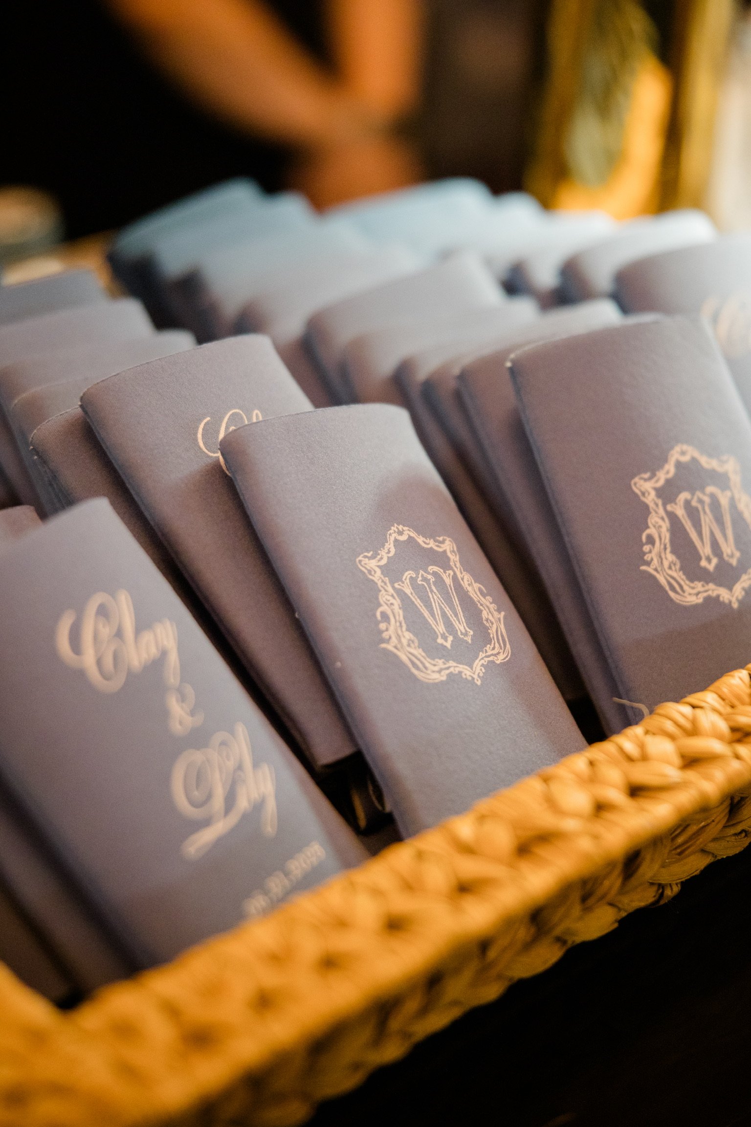 Multiple folded fabric swatches with monogram and decorative designs in a woven basket.