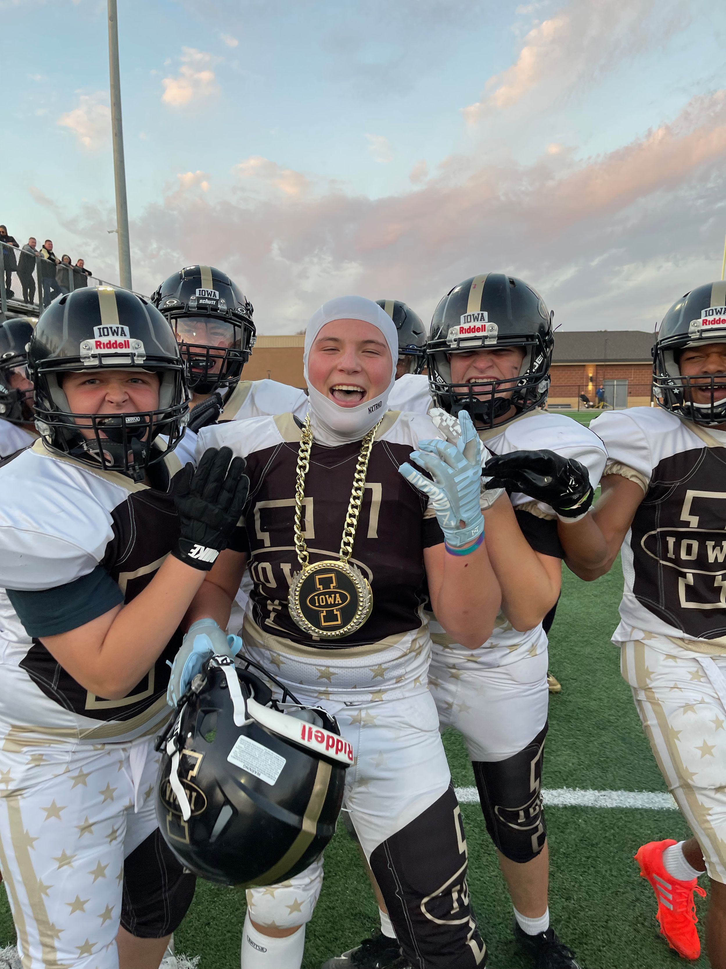 Group of football players in black and white uniforms celebrating on the field, with one player wearing a large medal around her neck, and smiling and waving at the camera.