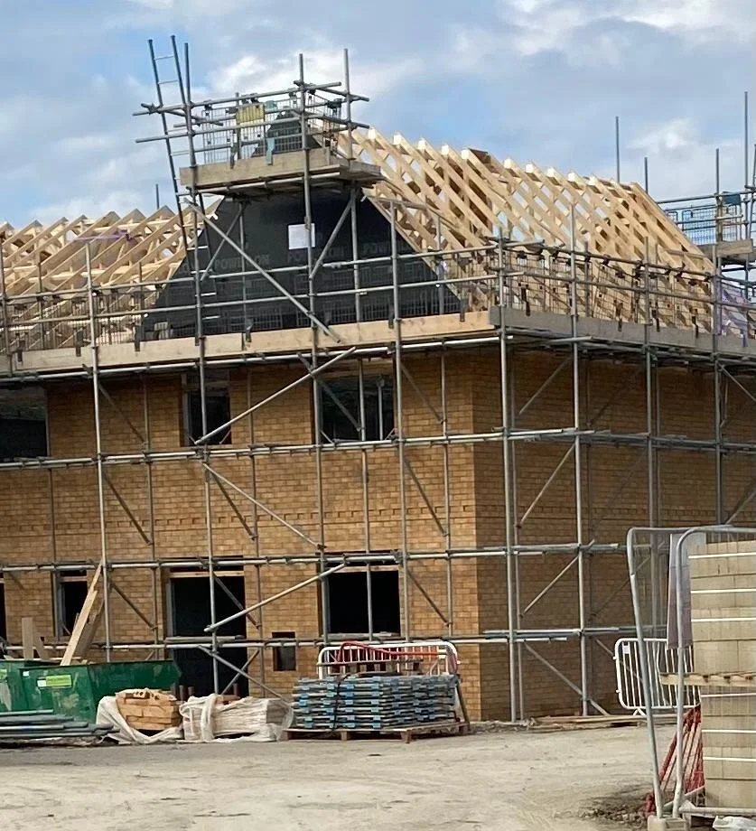Construction site with scaffolding around a brick building, in the process of installing a roof with wooden trusses.