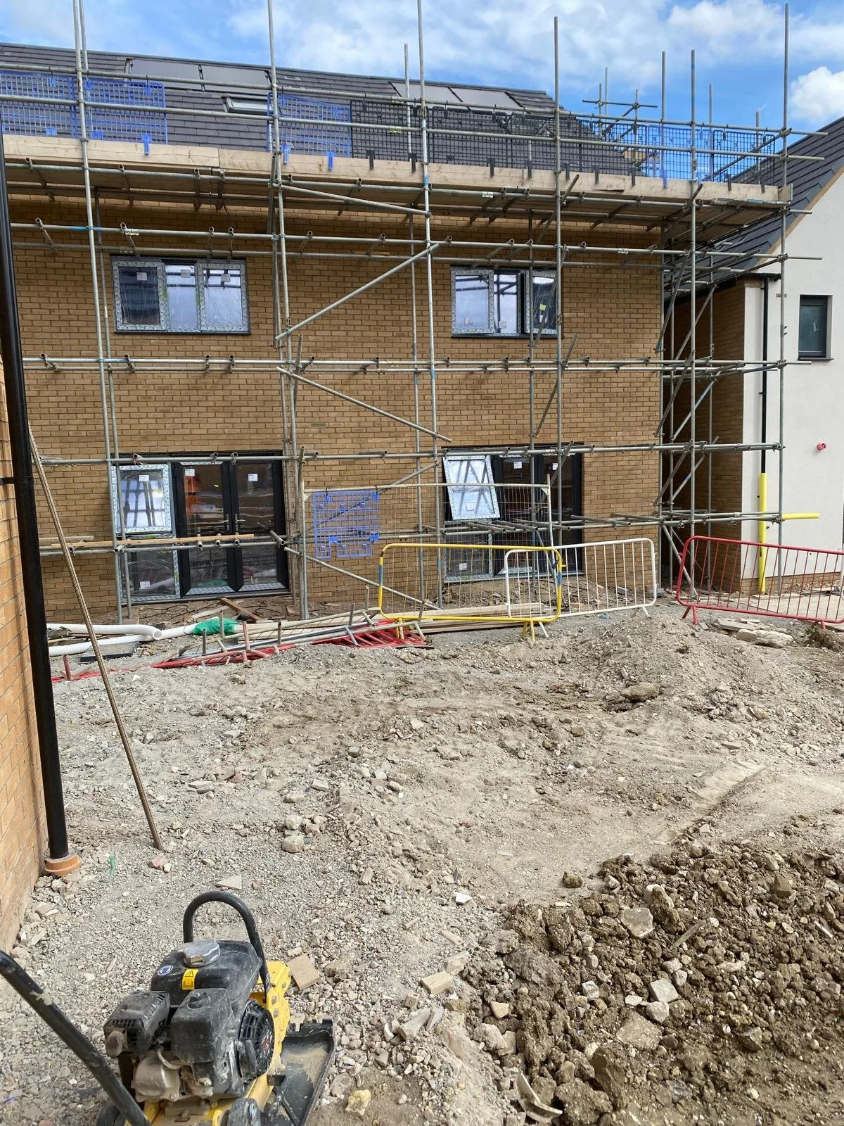 Construction site with a building under renovation, scaffolding surrounding it, and construction barriers on a dirt ground.