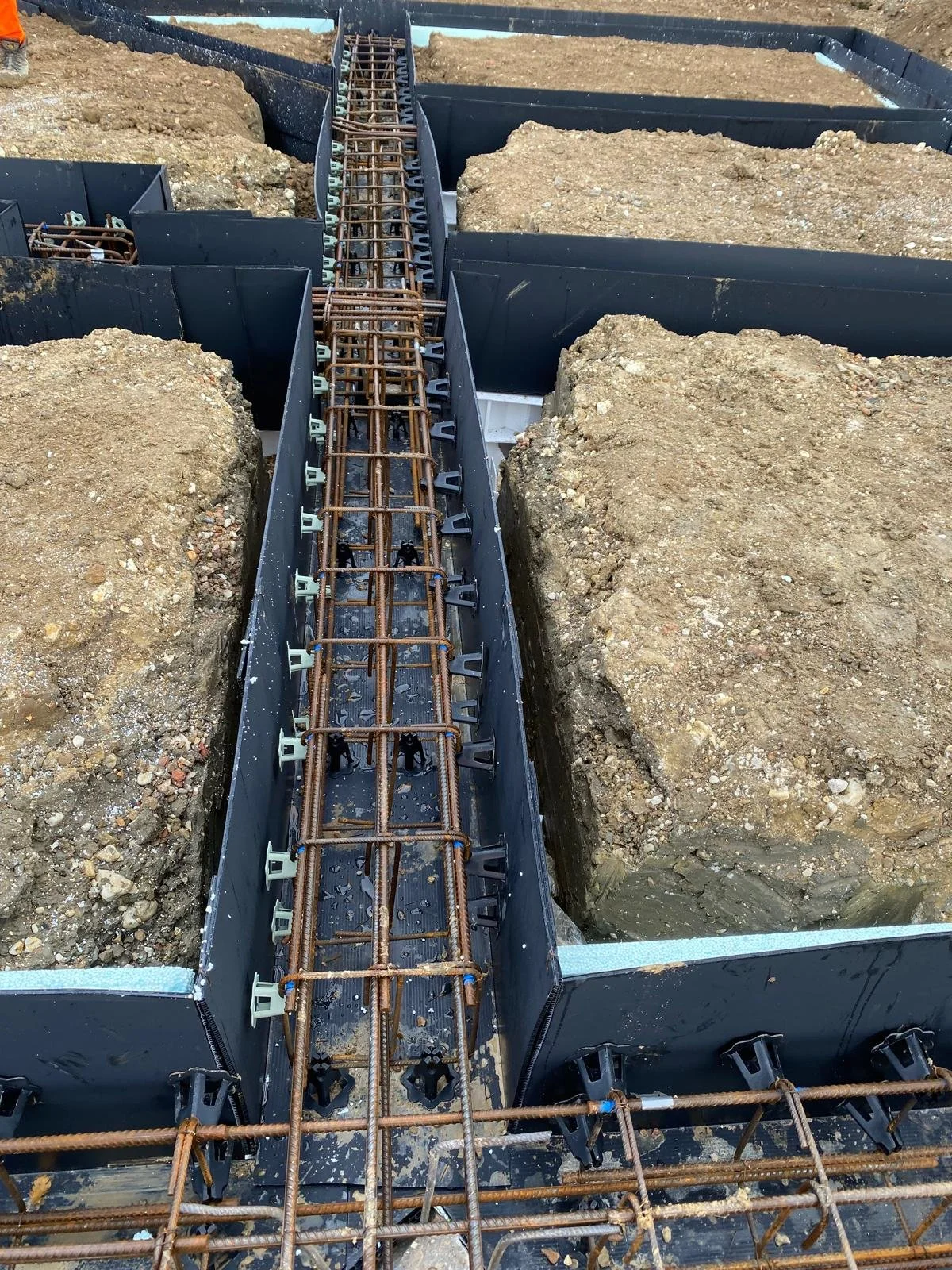 Construction site with rebar and forms set in trenches prepared for concrete pour.