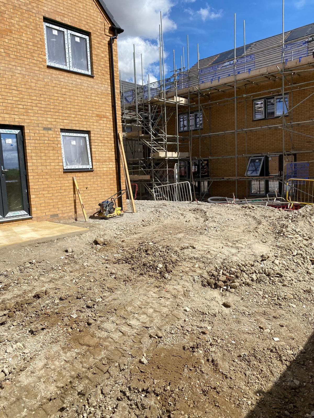 Construction site with building scaffolding, brick building, and exposed ground.