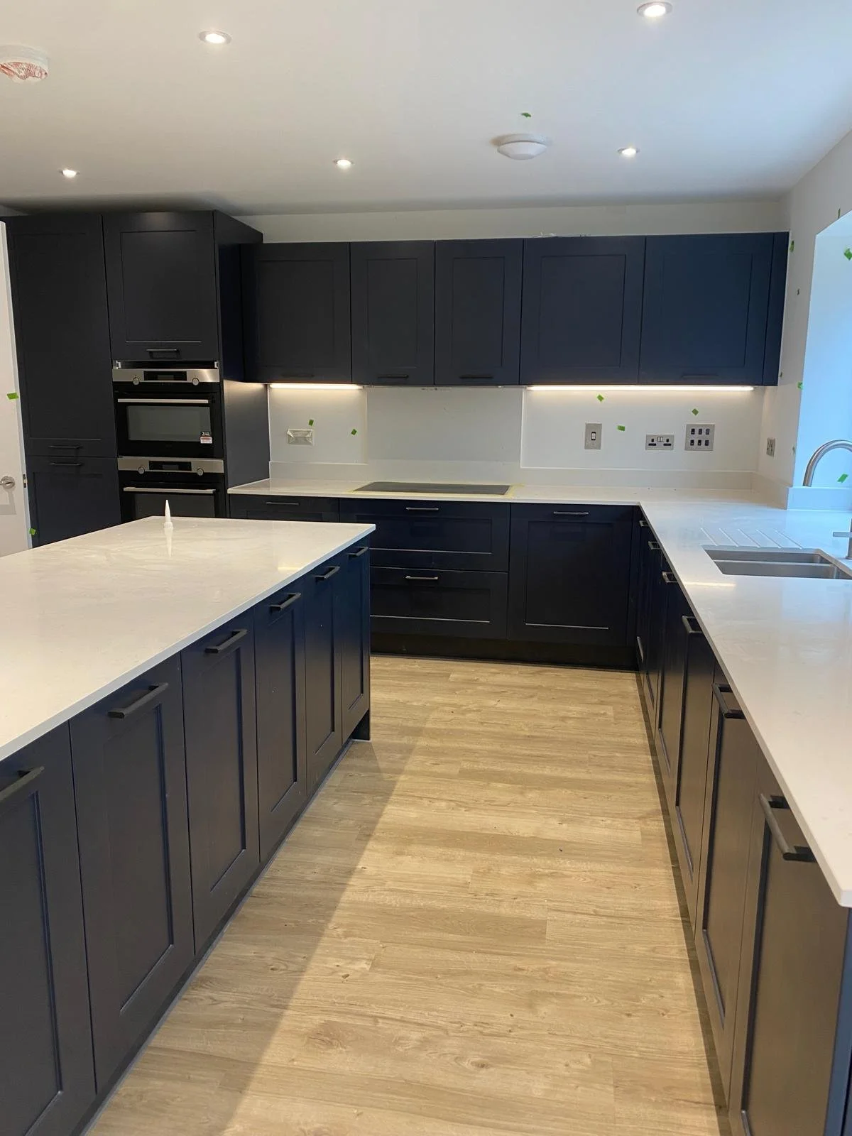 Modern kitchen with navy blue cabinets, white countertops, and wood-style flooring.