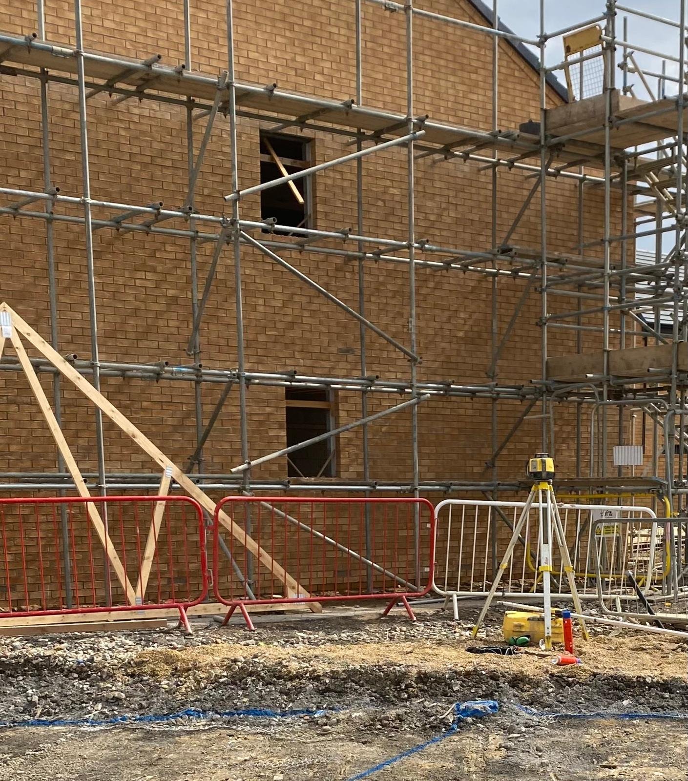 Construction site with scaffolding and orange safety barriers in front of a brick building under construction.