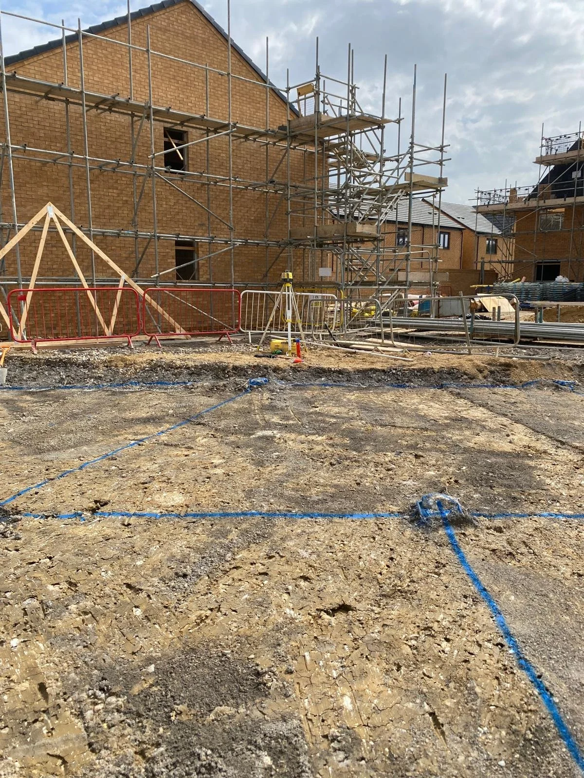Construction site with scaffolding around brick houses and blue chalk lines marking the ground.