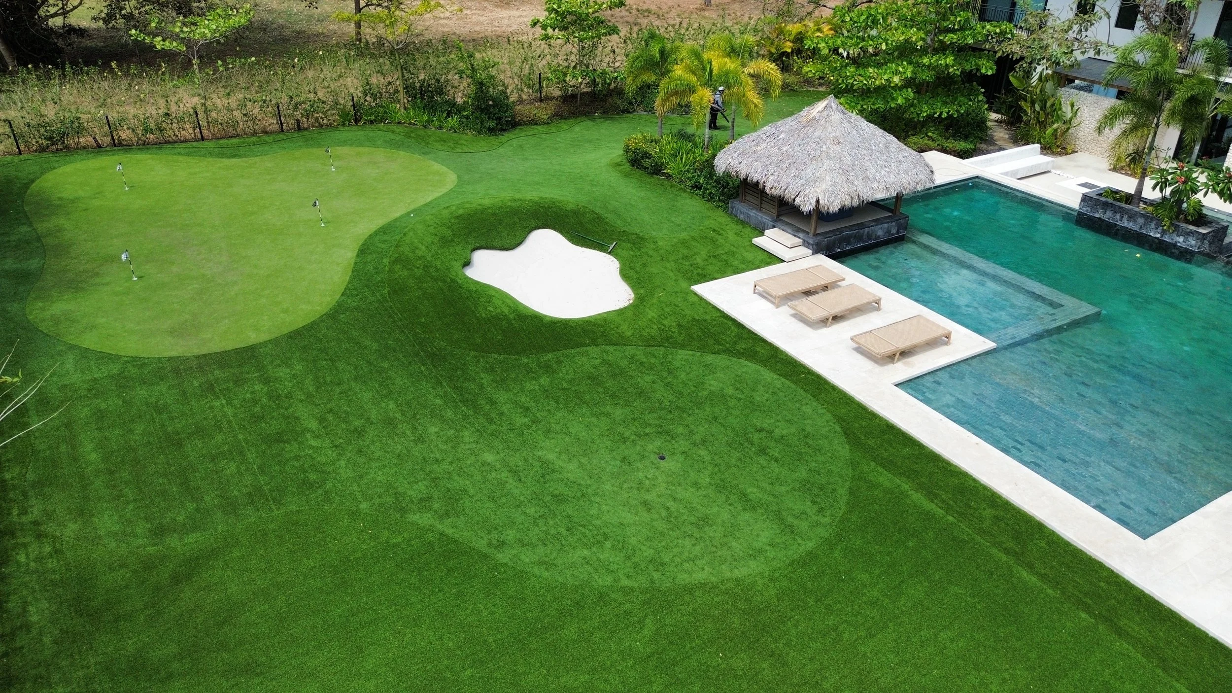 A backyard with a putting green, sand trap, and a swimming pool with lounge chairs under a thatched-roof cabana in guanacaste costa rica. Putting green and a pet odor free dog solution
