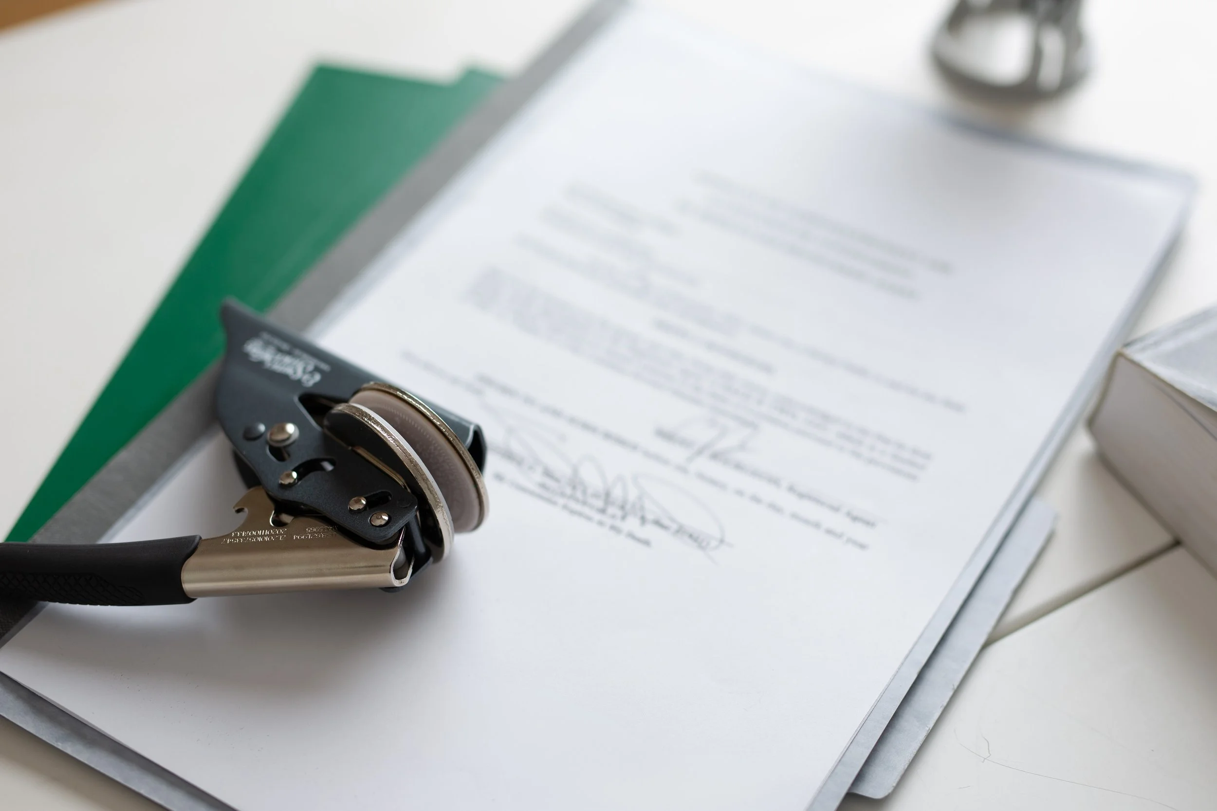 A document on a clipboard, with a metal hole punch and a green folder on a white surface.