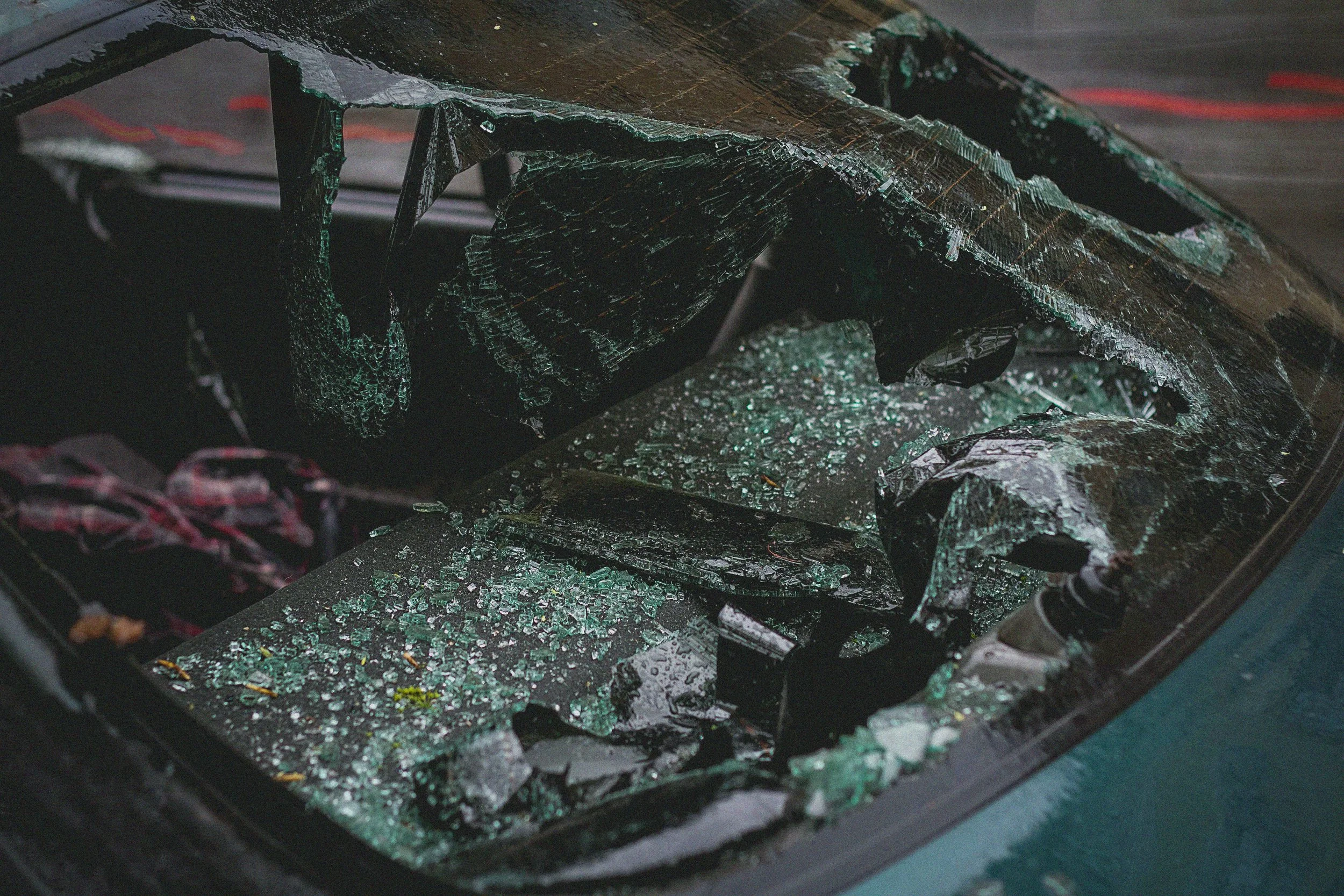 The image shows a close-up view of a shattered car windshield with broken glass splattered across the surface inside the vehicle.