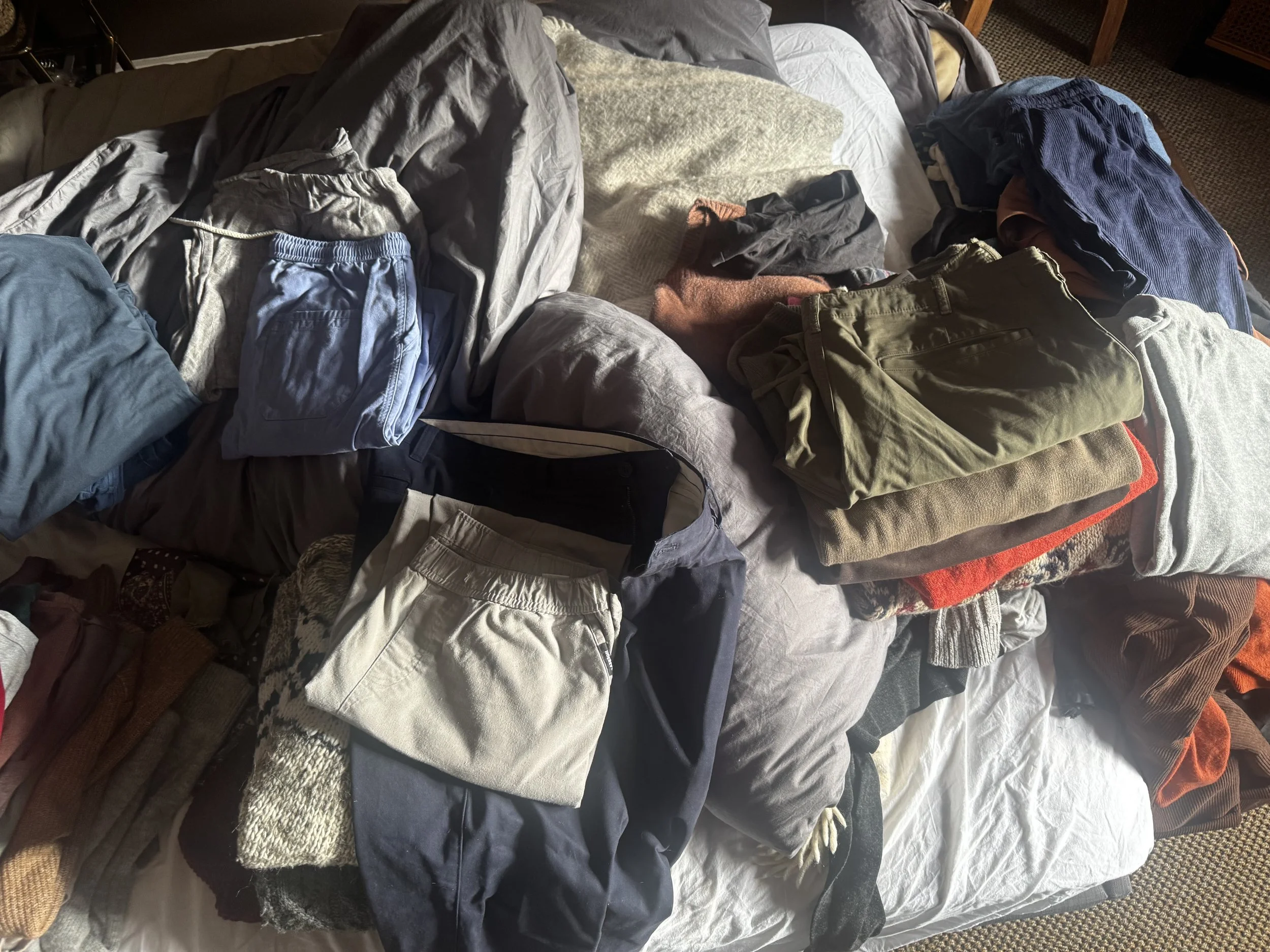 A bed with various clothes and towels laid out on it, including shorts, pants, shirts, and a towel, in a disorganized manner.
