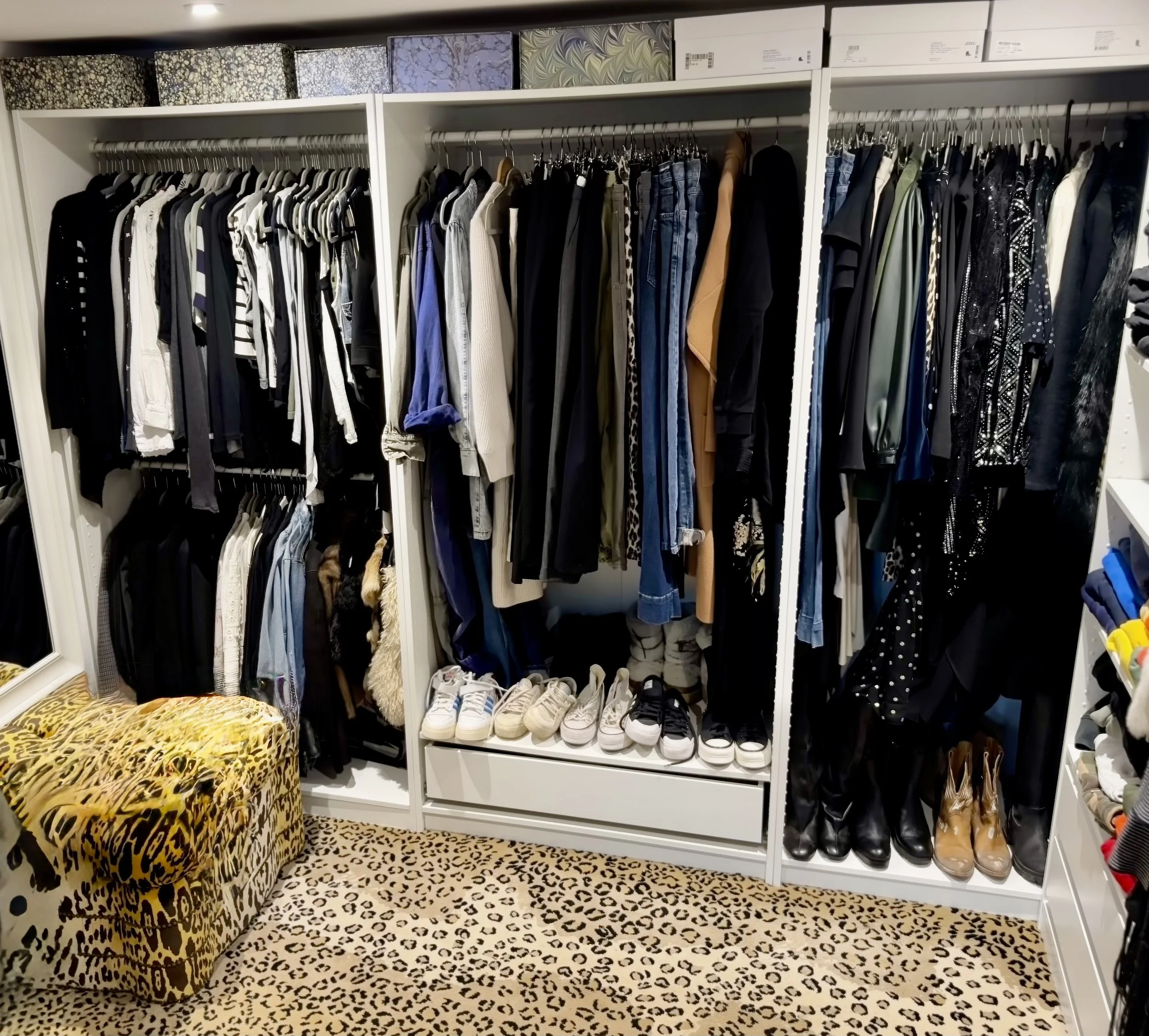 Closet with clothing on hangers, shoes on shelves, and a leopard print bench on a leopard print carpet.