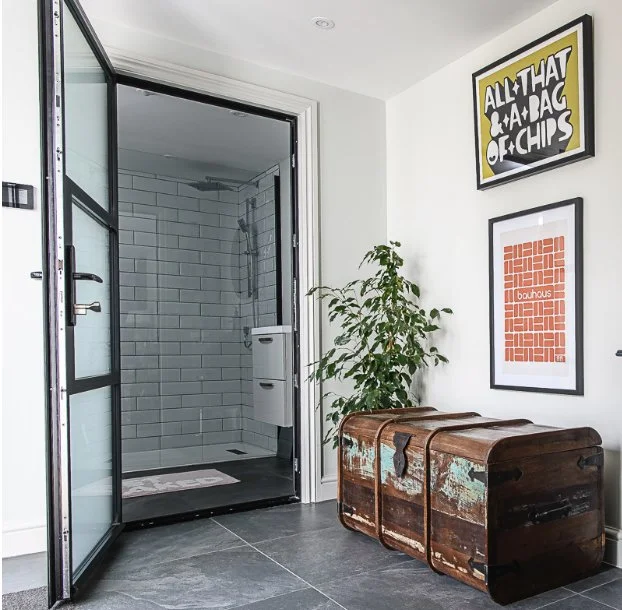 Interior of a bathroom with a walk-in shower, a potted plant, and vintage wooden chest, decorated with framed artwork on the wall.
