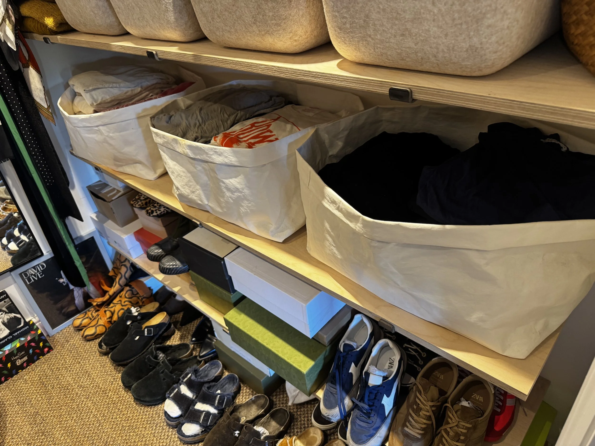 Shelves with fabric bins containing clothes and accessories, and a lower area with various shoes and shoe boxes.