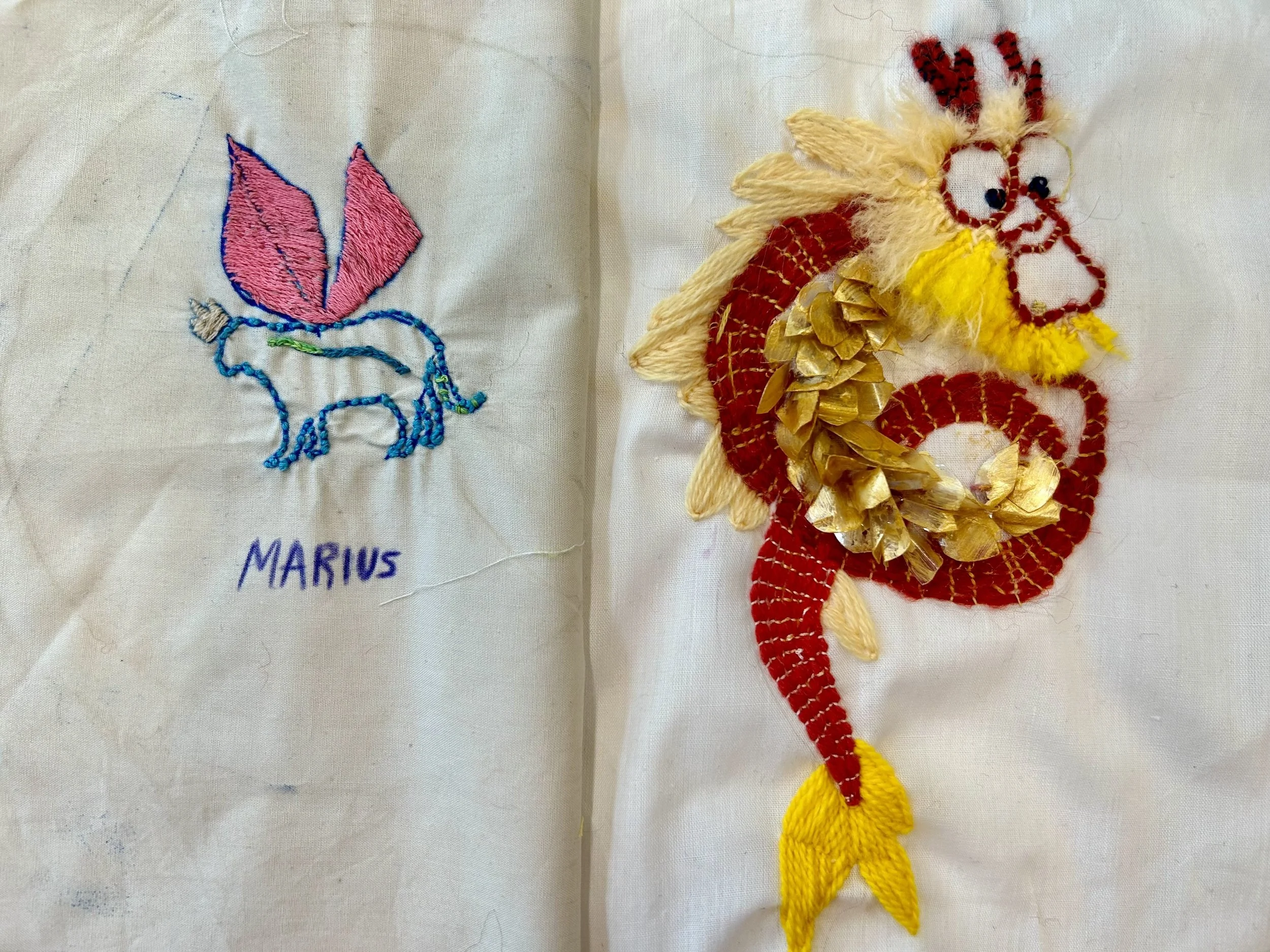 Embroidery of a dragon with yellow, red, and golden embellishments, alongside a fabric piece with colorful stitched animal and the name 'MARIUS'.