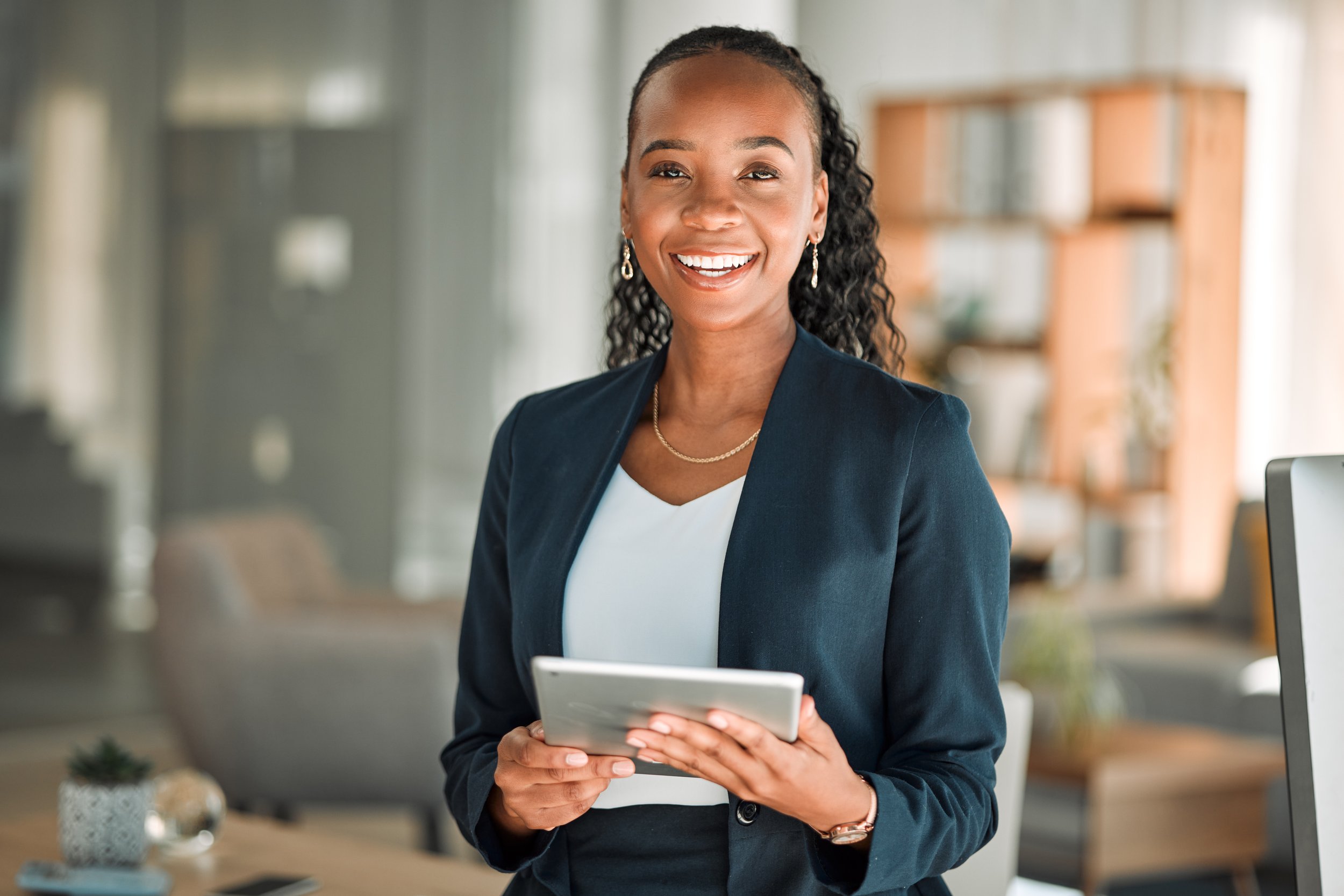 Smile of a woman in professional attire holding a tablet in a modern office.