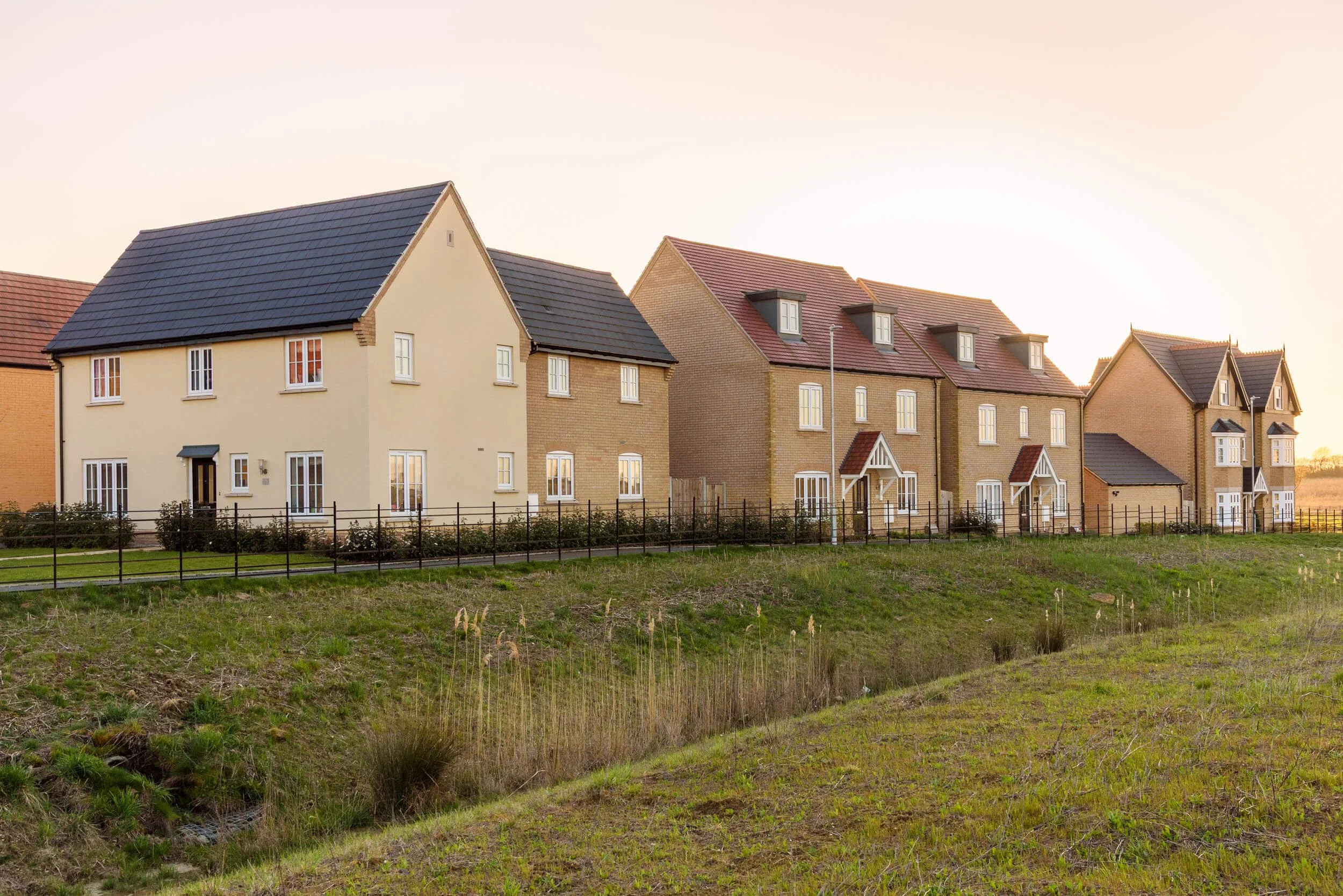 Row of modern residential houses with front yards and black fencing, taken during sunset.