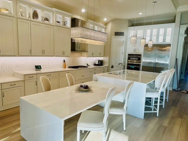 Modern kitchen with white cabinets, a large island with seating, stainless steel appliances, and decorative lighting fixtures.
