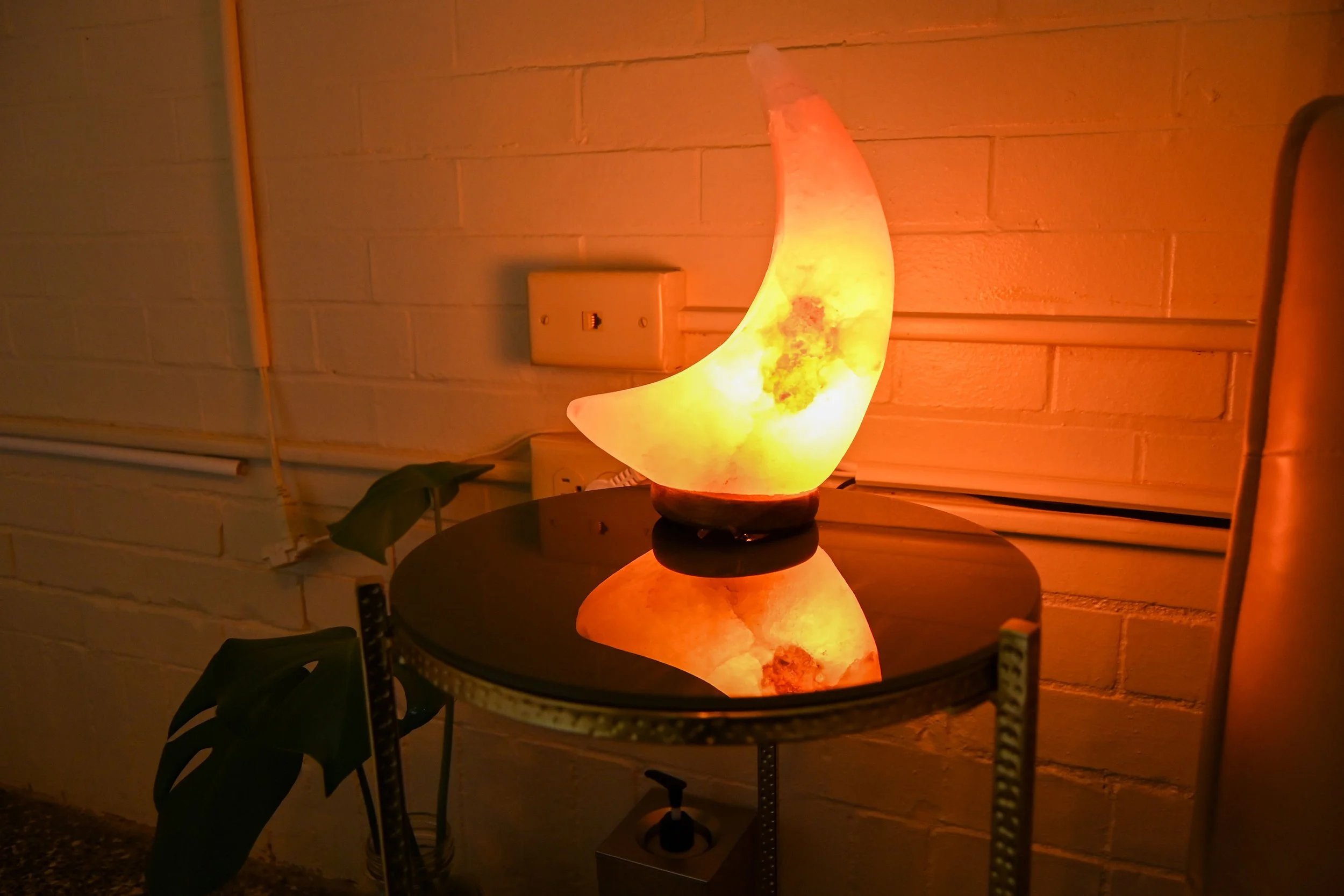 TREATMENT ROOM: Client seat and side table area with soft-glowing moon-shaped salt lamp