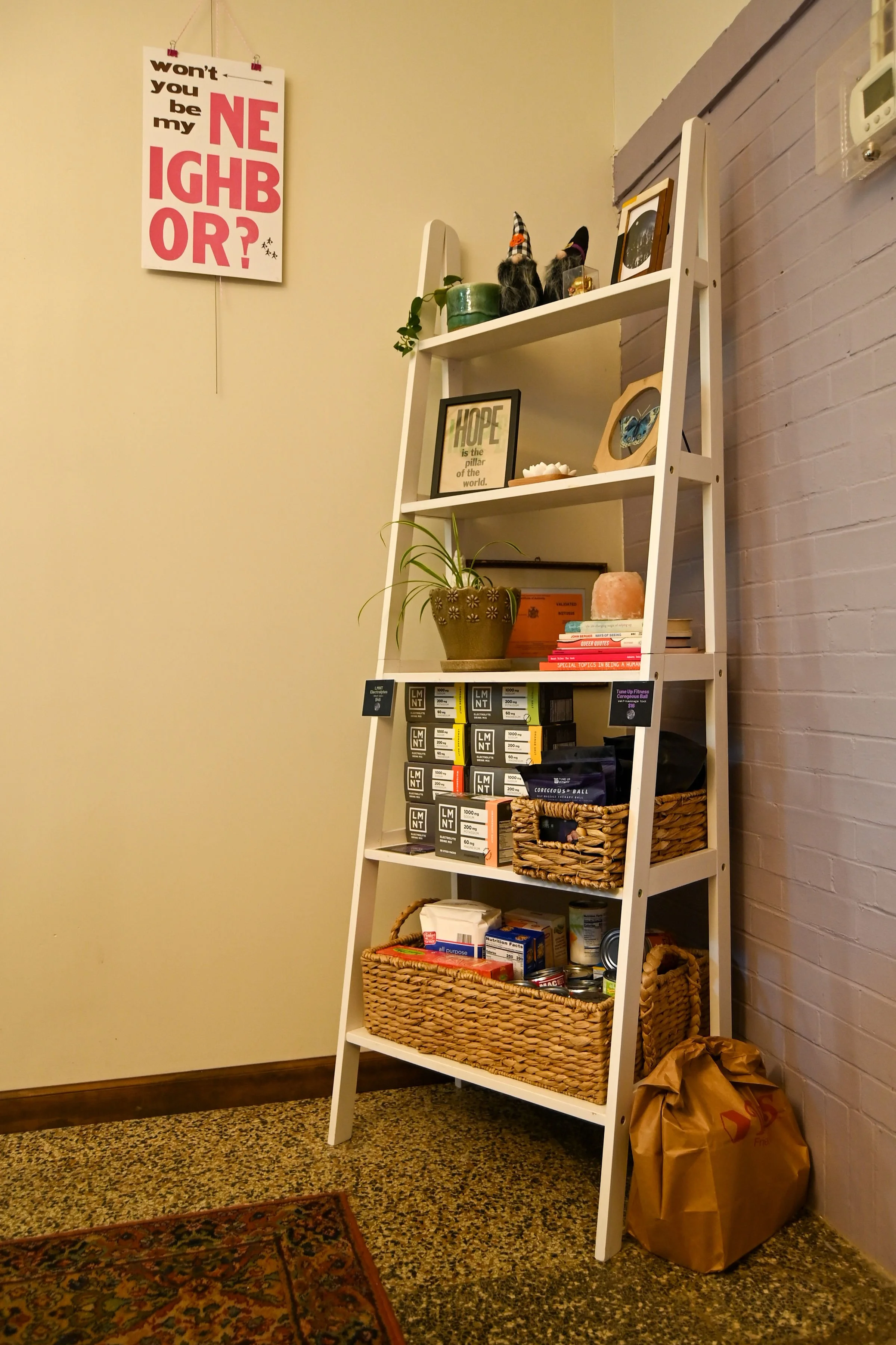 OFFICE: Shelf in waiting room that stores Good Moon's recommended supplements like electrolytes and self-massage tools as well as food pantry donations.