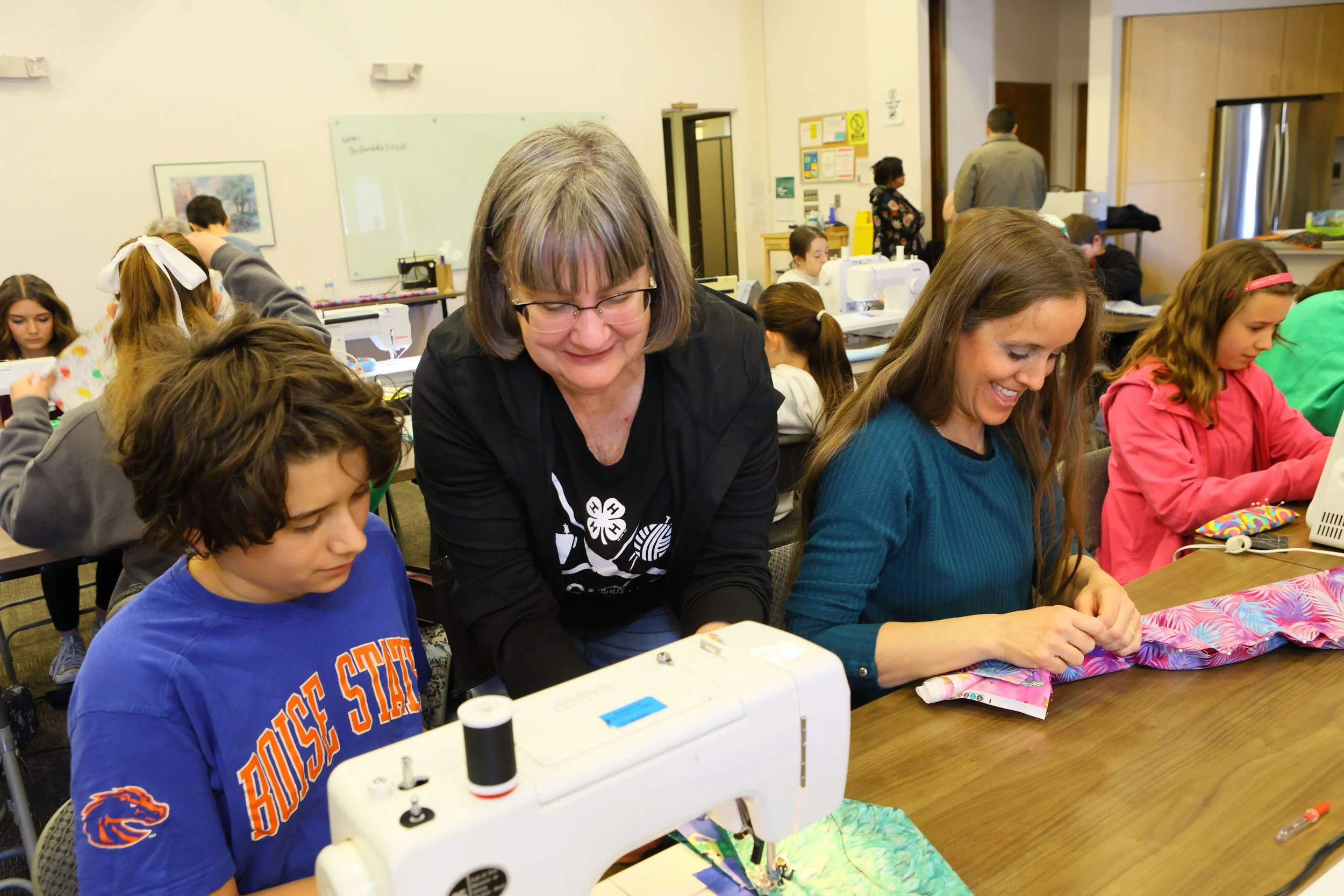 Children and Celia sewing in a classroom with sewing machines and fabric.