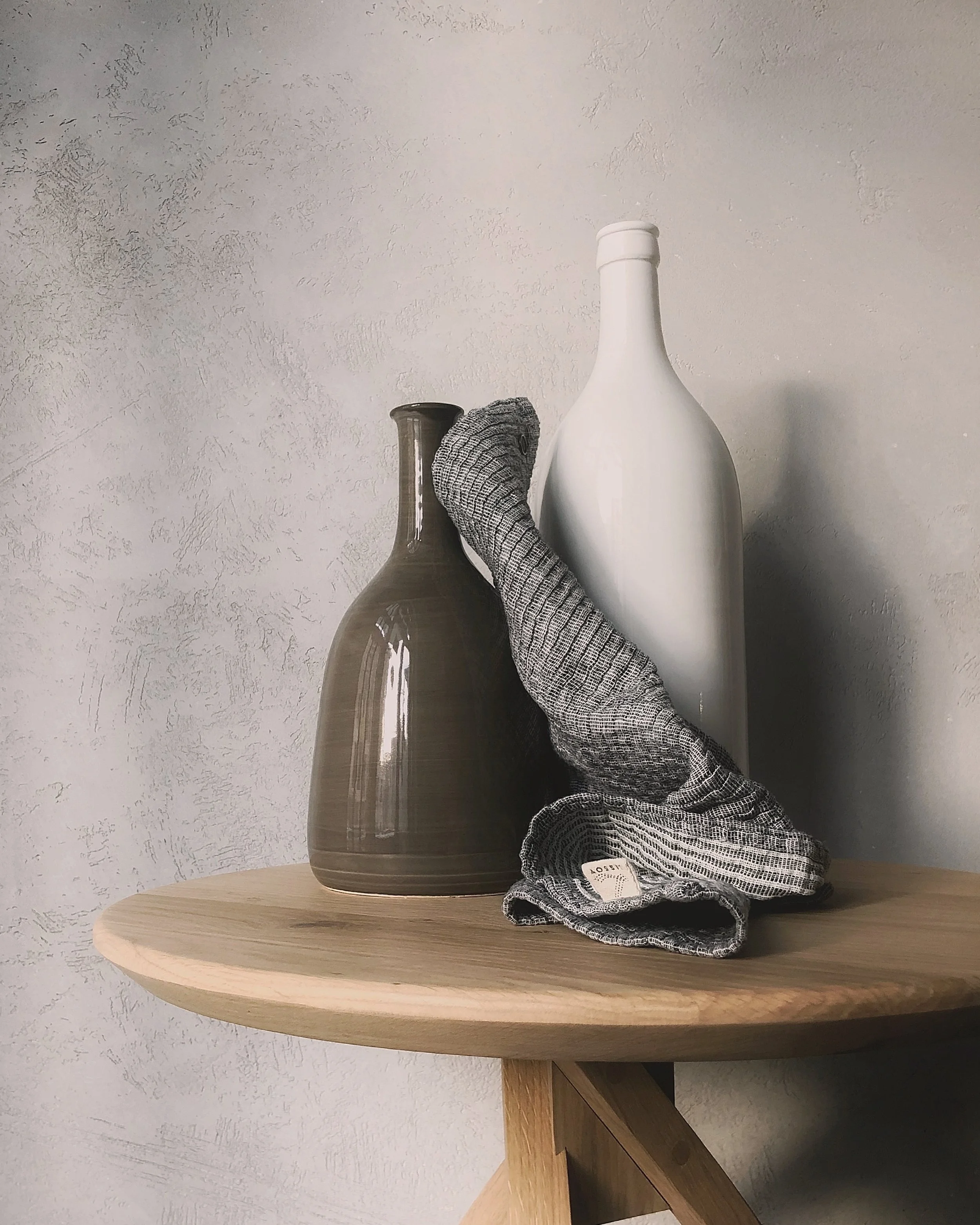 Two vases, one brown and one white, and a gray striped sock on a wooden table against a textured wall.