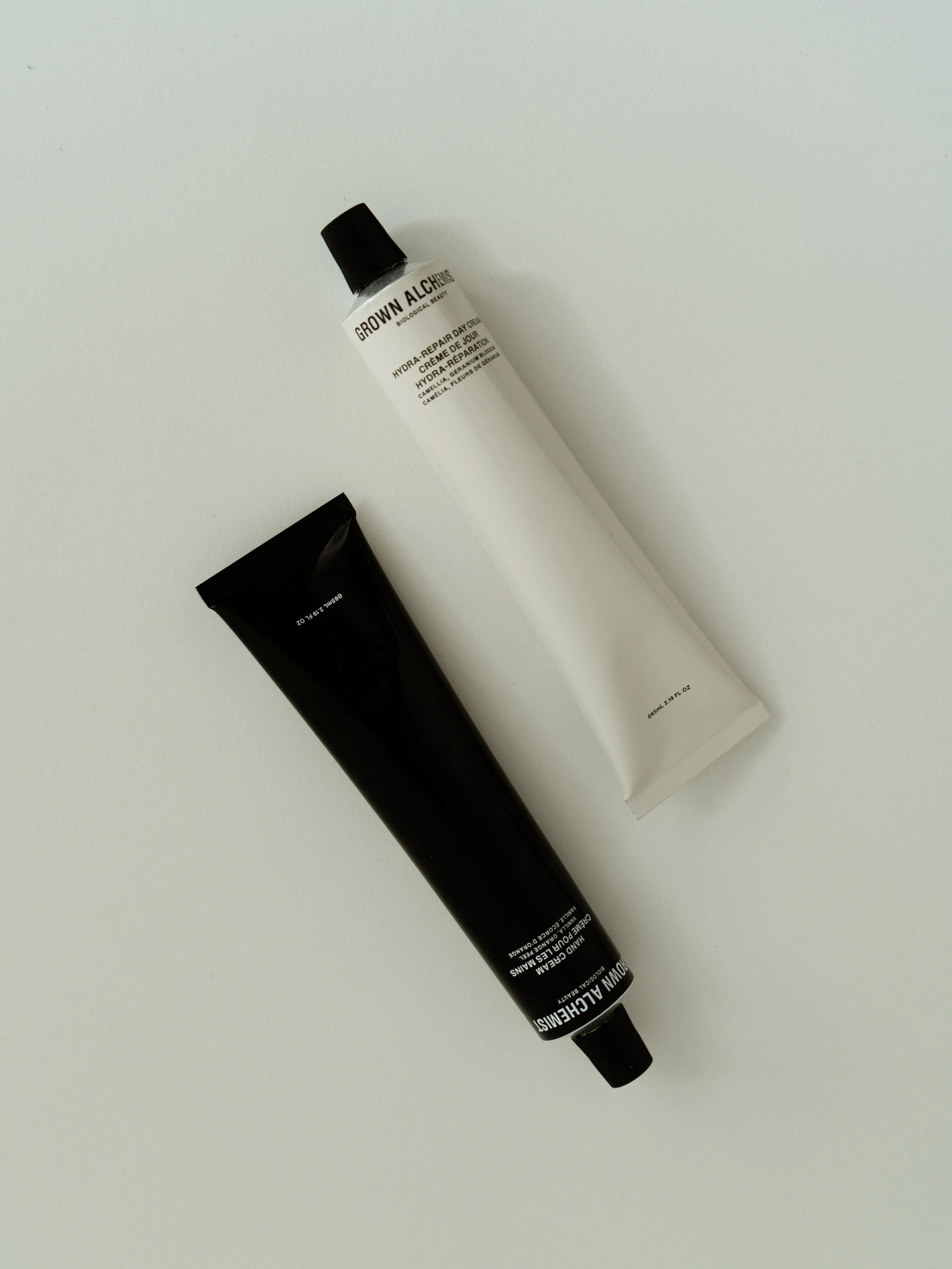 Two tubes of skincare product, one white and one black, lying on a white surface.