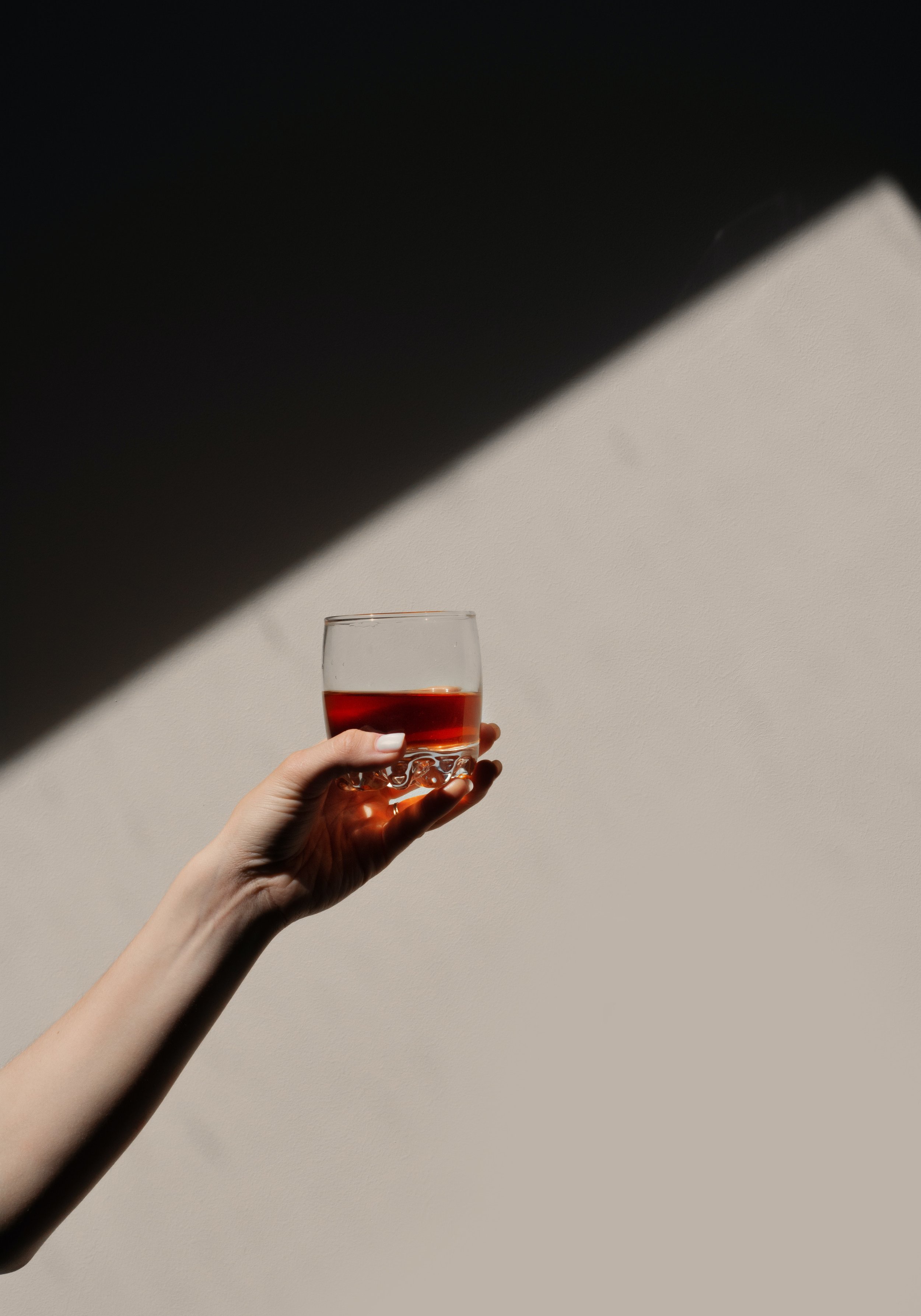 Person holding a glass of red wine against a background with shadows and light.