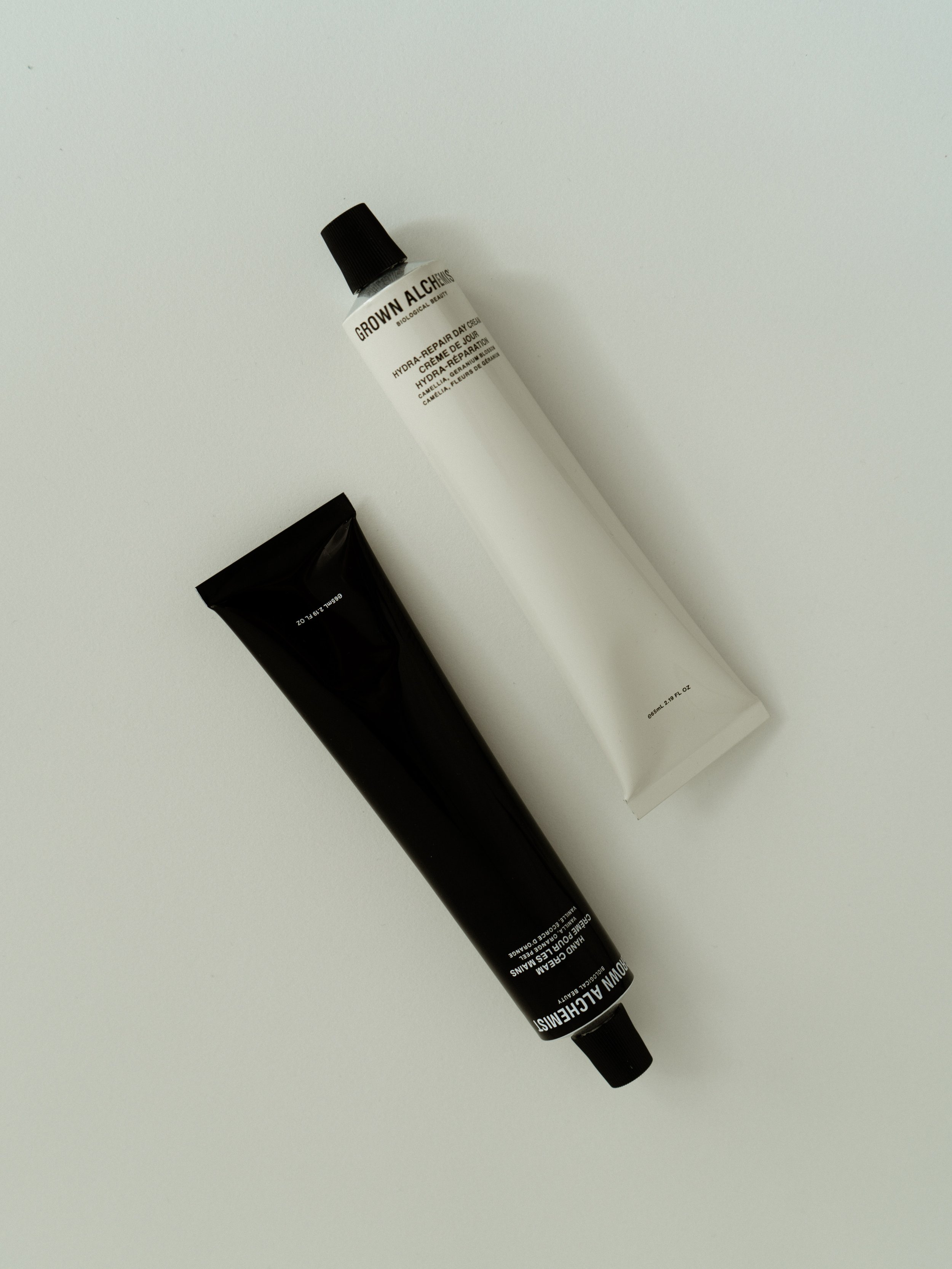 Two tubes of skincare cream, one black and one white, placed diagonally on a white surface.