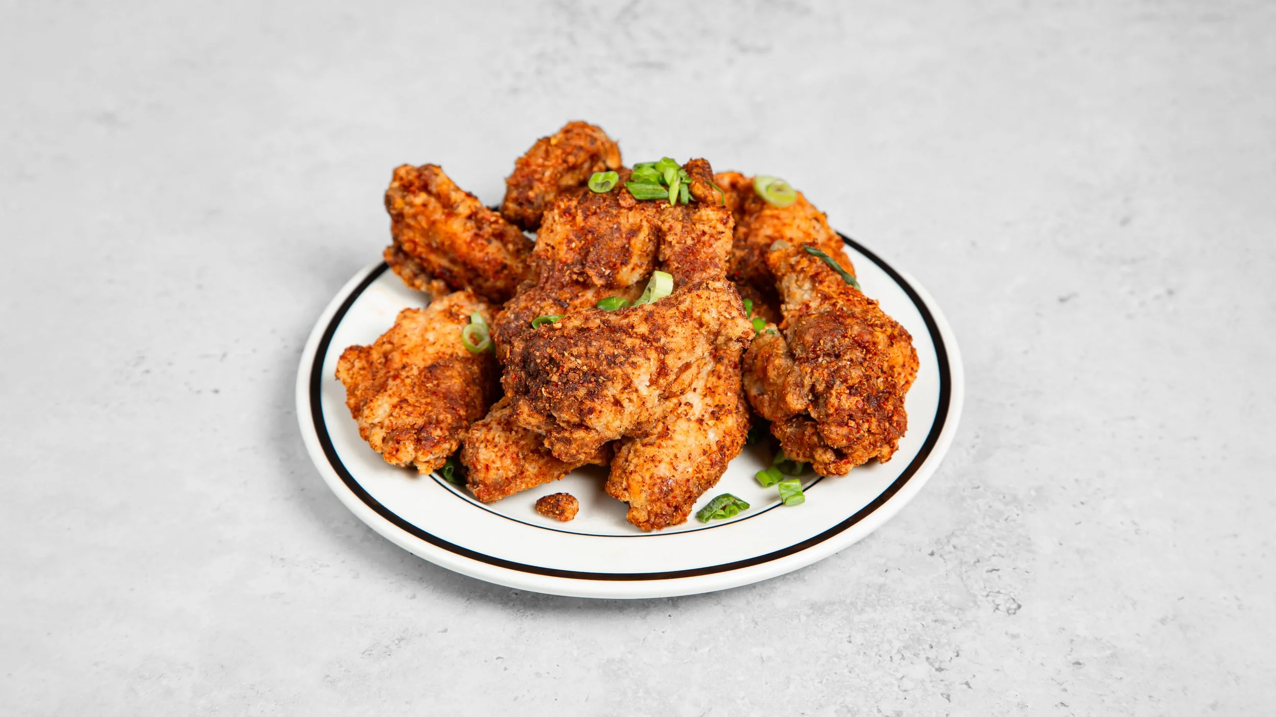 Taiwanese Fried chicken wings garnished with chopped green onions on a white plate with black rim