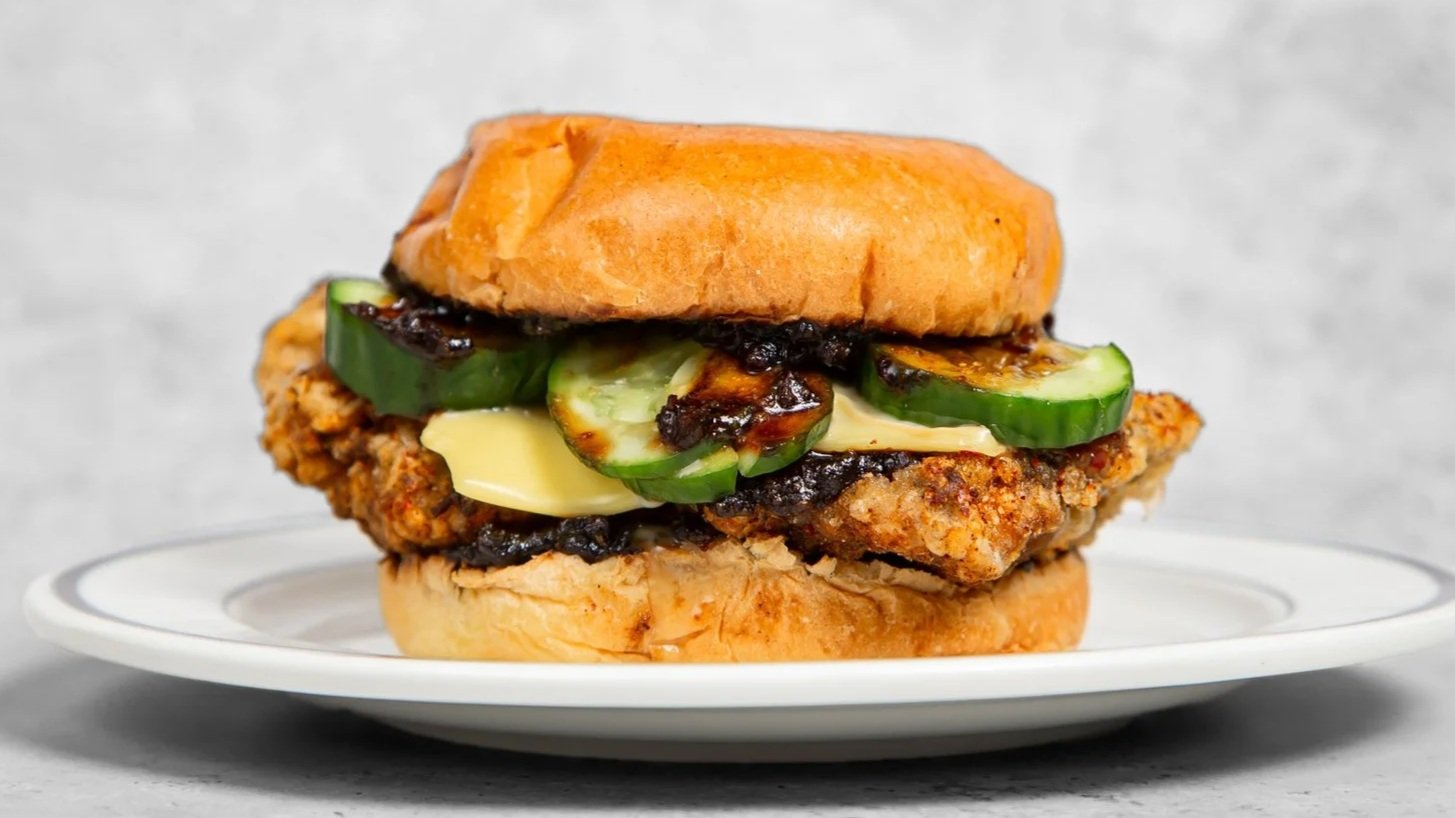 Crispy fried chicken burger with chilli oil pickles, cheese, and raohe pepper gravy sauce on a bun served on a white plate