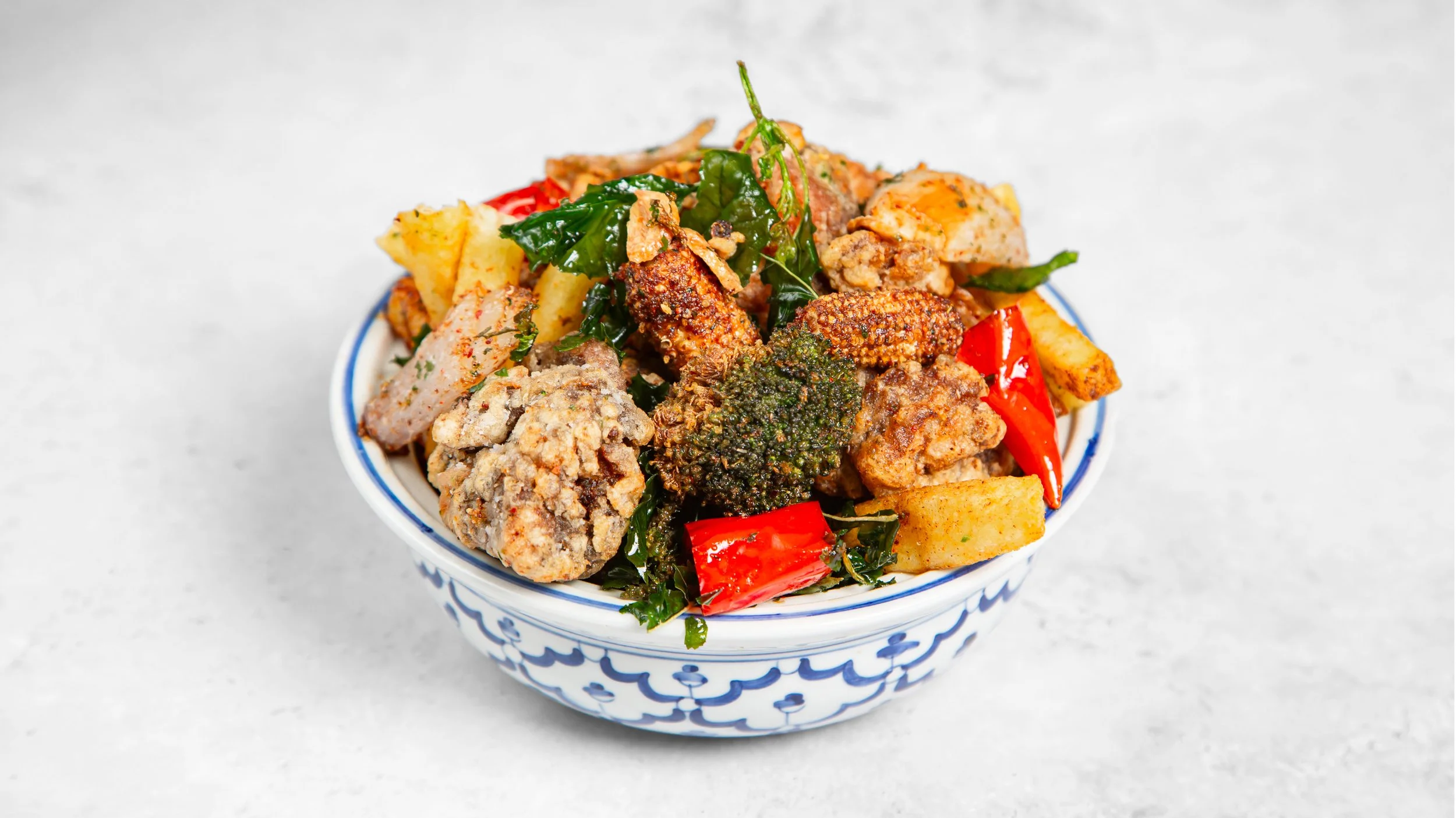 A bowl of fried chicken pieces, broccoli, red chilli peppers, fries, and basil. Known in Taiwan as Yan Su Ji, an authentic version of the Irish Spice Bag in London.
