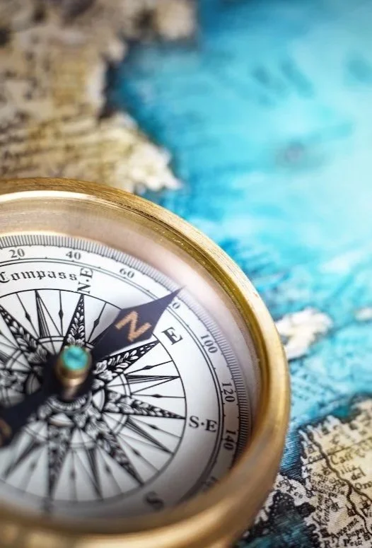 Close-up of a brass compass on a colorful map with blue and beige tones.