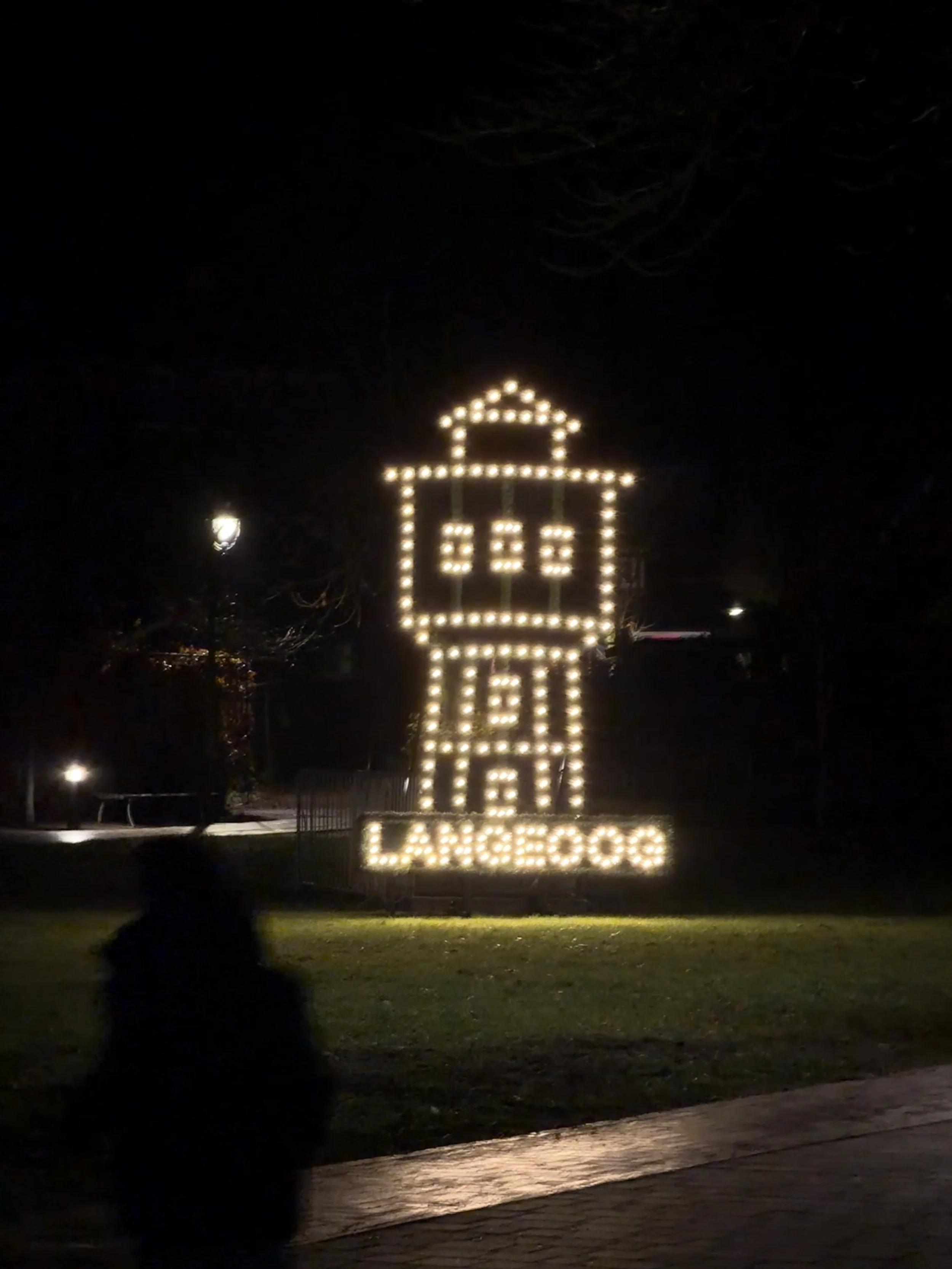 Lichterkonstruktion eines Leuchtturms mit dem Wort 'LANGHOUT' darunter auf einer Wiese bei Nacht.