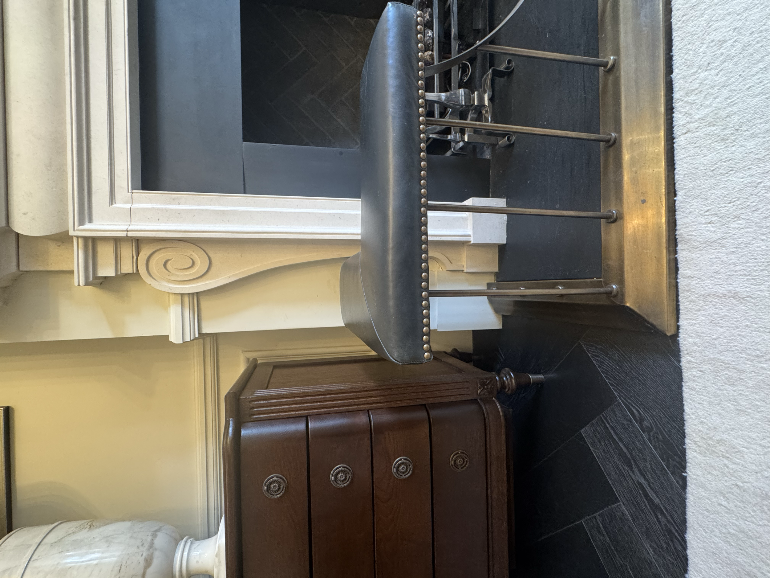 Modern indoor fireplace with a white marble mantel, black hearth, and a set of chrome and black fireplace tools on a brass stand.