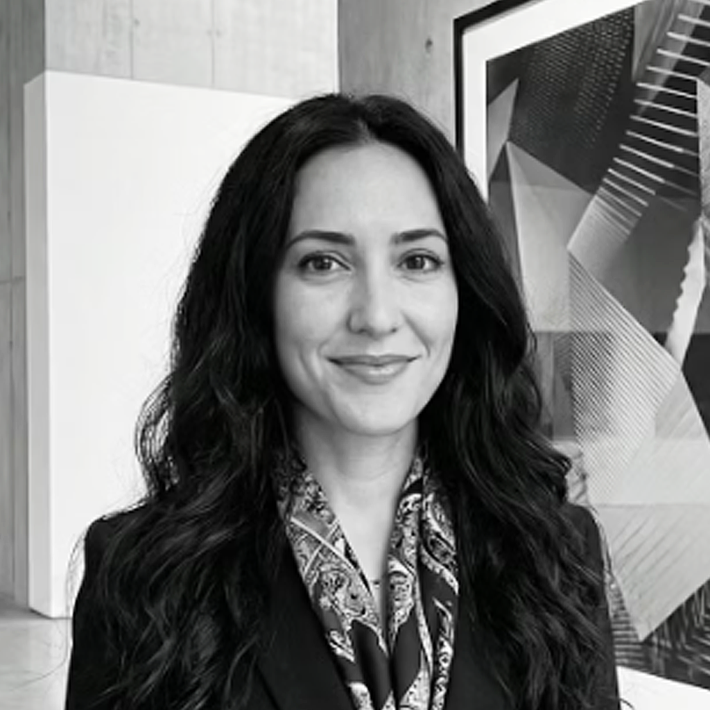 Black and white portrait of a woman with long wavy hair, smiling, standing indoors with modern artwork in the background.